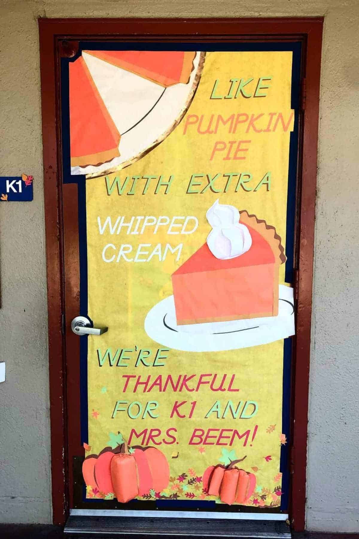 Classroom door decorated with images of pumpkin pie, whipped cream, and pumpkins, featuring the text: "Like pumpkin pie with extra whipped cream, we're thankful for K1 and Mrs. Beem!.