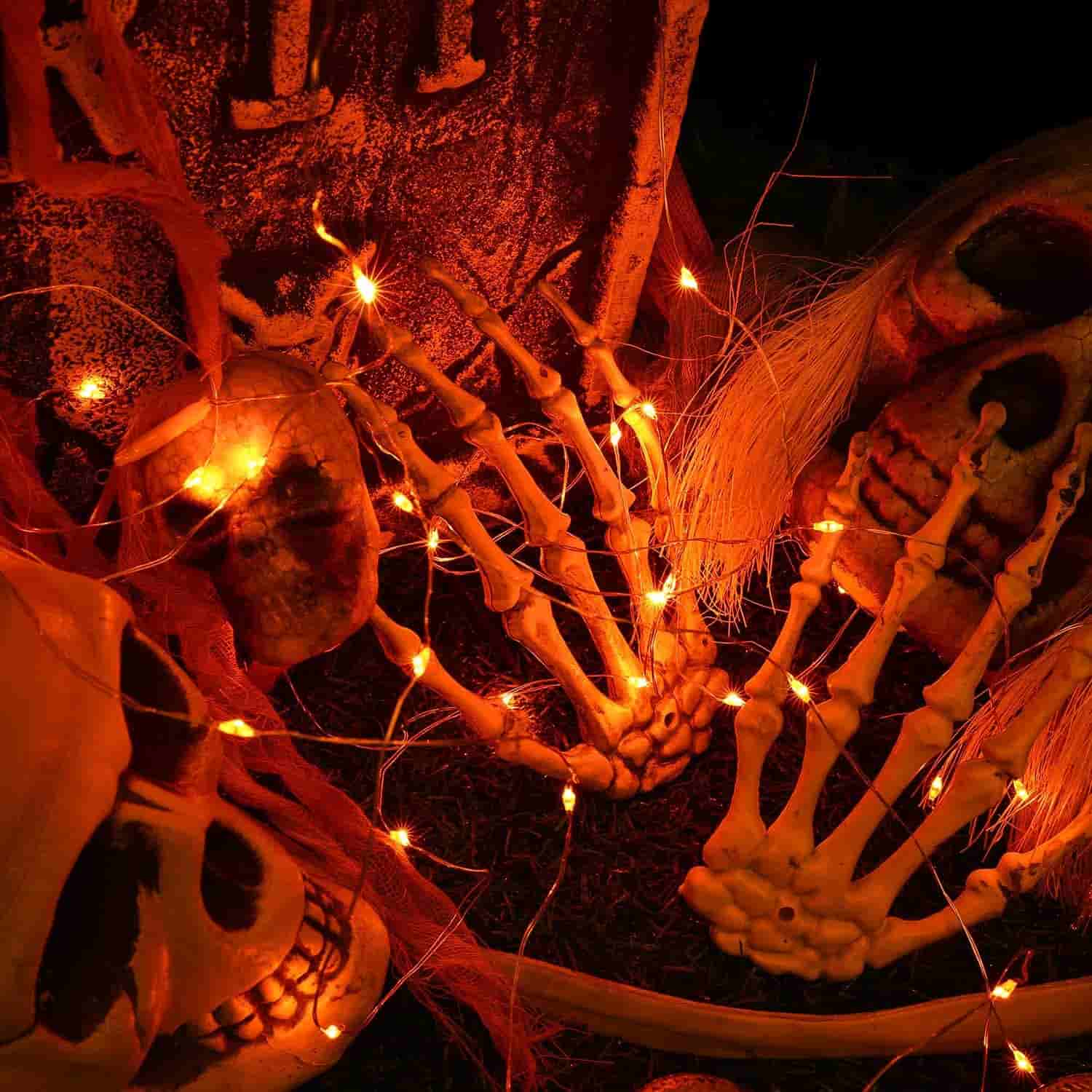 Plastic skeleton hands, skulls, and orange string lights arranged together in a Halloween-themed display.