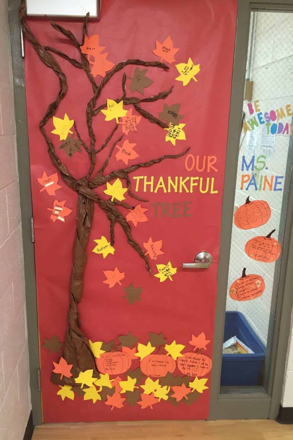 Classroom door decorated with a brown paper tree and colorful paper leaves, each labeled with things students are thankful for. The words "Our Thankful Tree" are displayed in large letters.