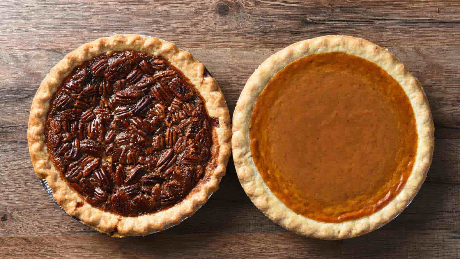 Two pies on a wooden surface: one pecan pie with a nut topping on the left, and one smooth pumpkin pie on the right.