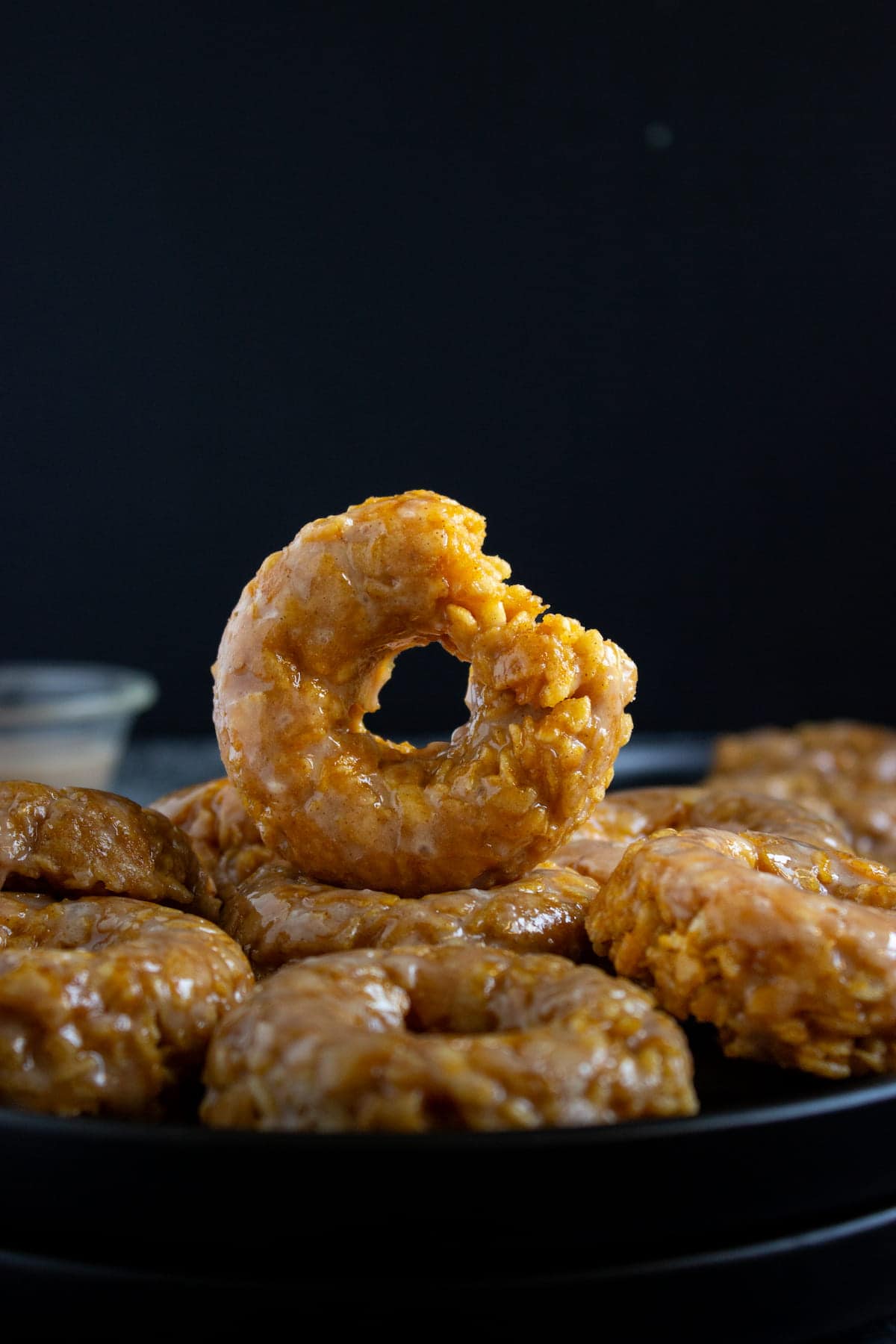 A stack of glazed, round cookies are displayed on a dark surface, with one cookie resting upright on top of the others.