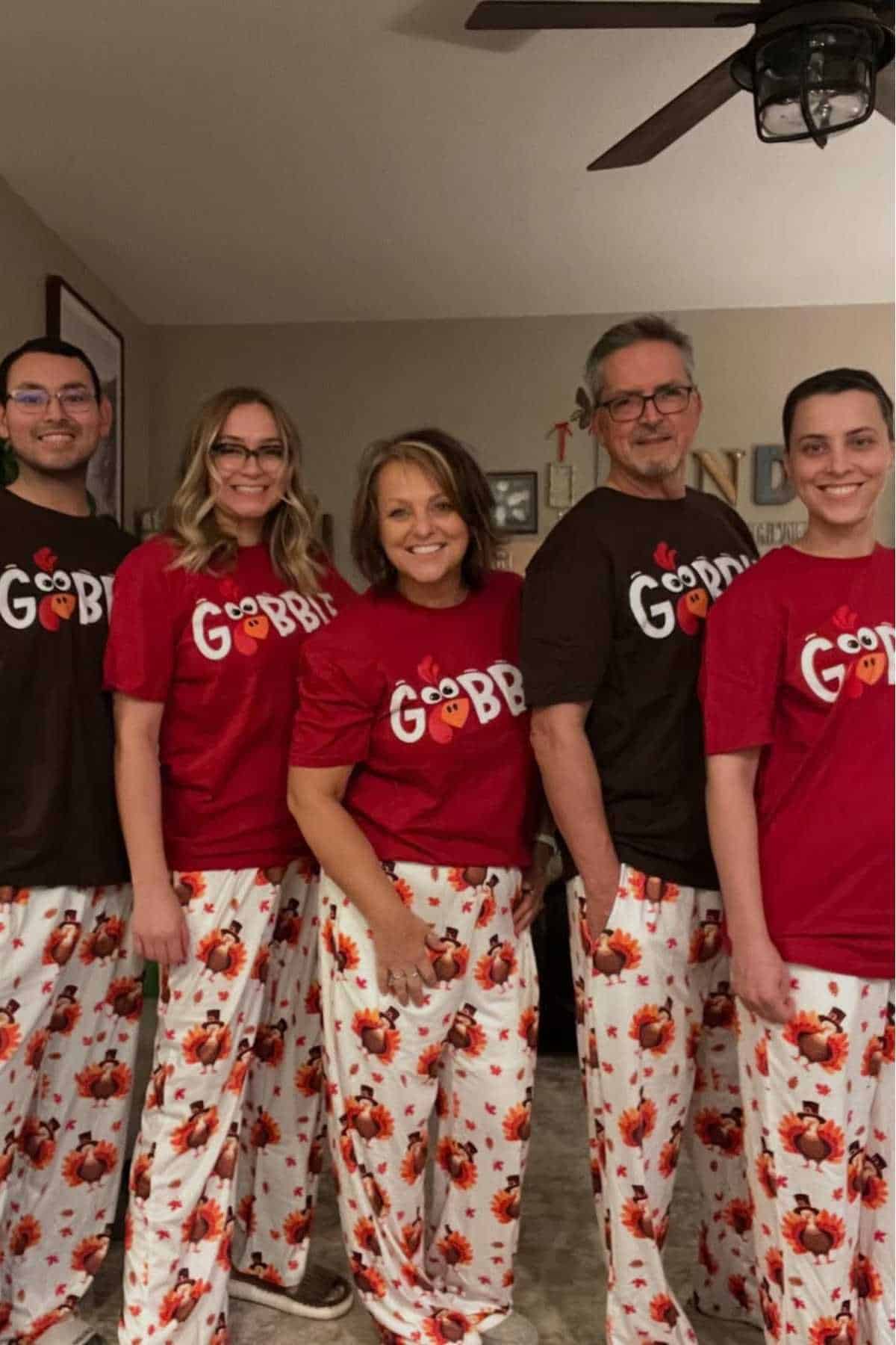 Five people stand indoors wearing matching turkey-themed pajamas; three wear red "Gobble" shirts and two wear brown "Gobble" shirts.