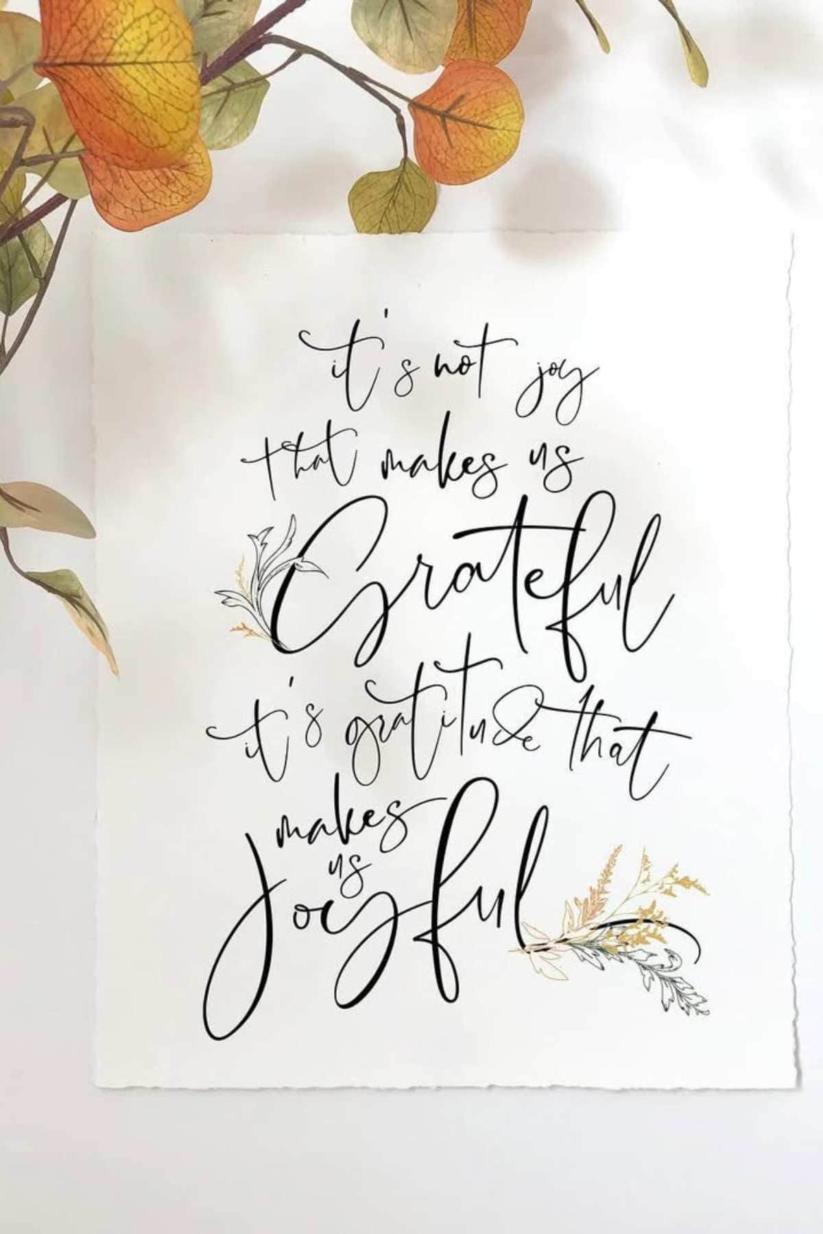 A handwritten sign reads, "It’s not joy that makes us grateful, it’s gratitude that makes us joyful," with decorative leaves in the corner and autumn leaves above.