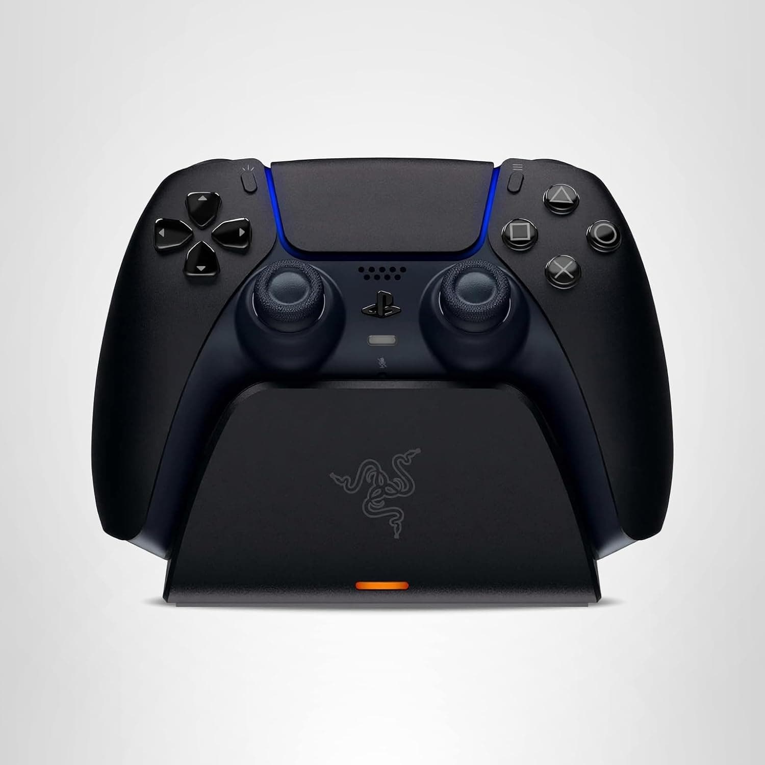 A black gaming controller sits on a matching charging dock with a small orange indicator light on the front.