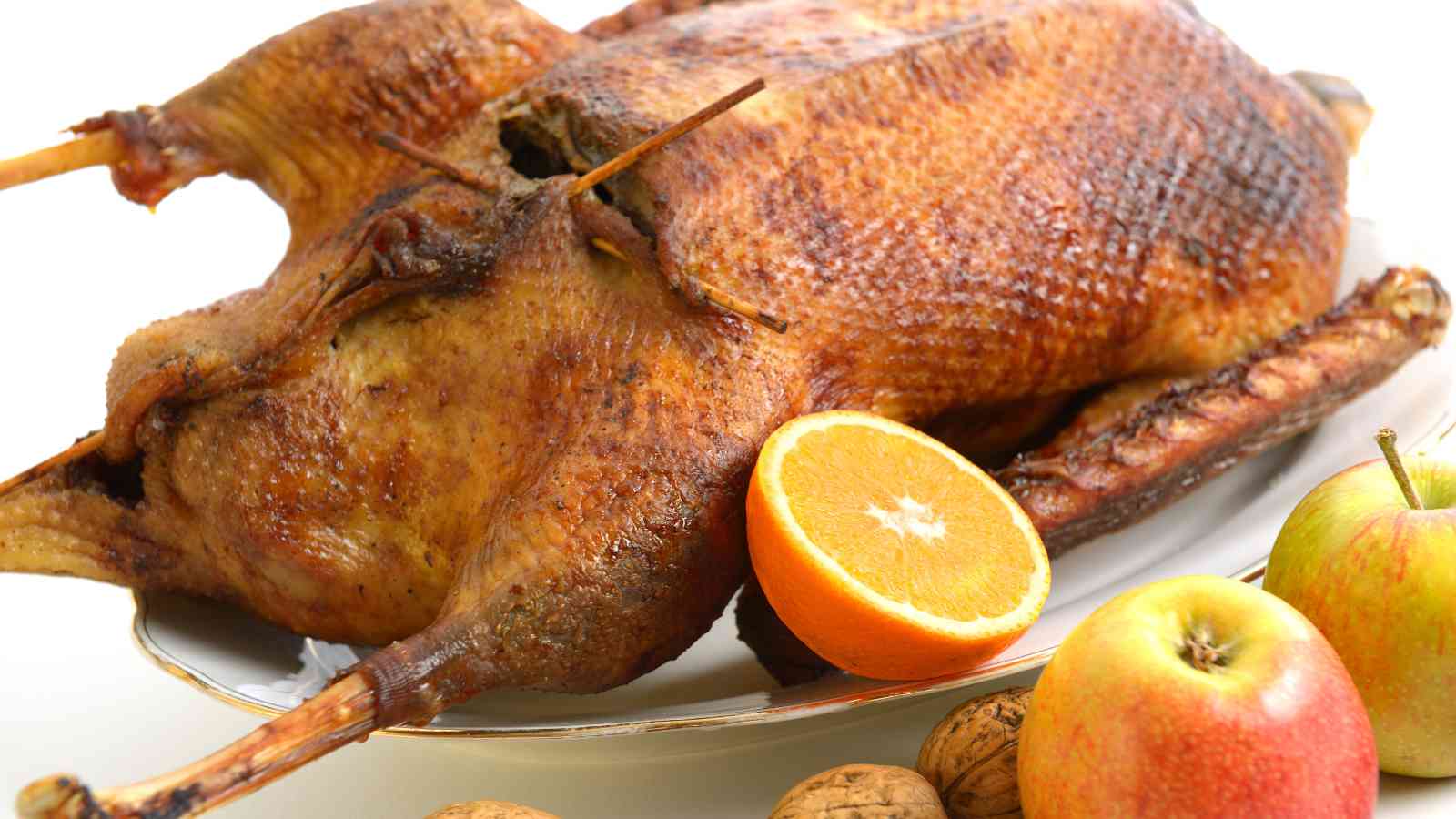 Roast whole goose served on a platter with a halved orange, apples, and walnuts.