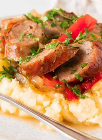 Ready-to-serve oven-roasted sausage on a white plate with a fork resting on it.