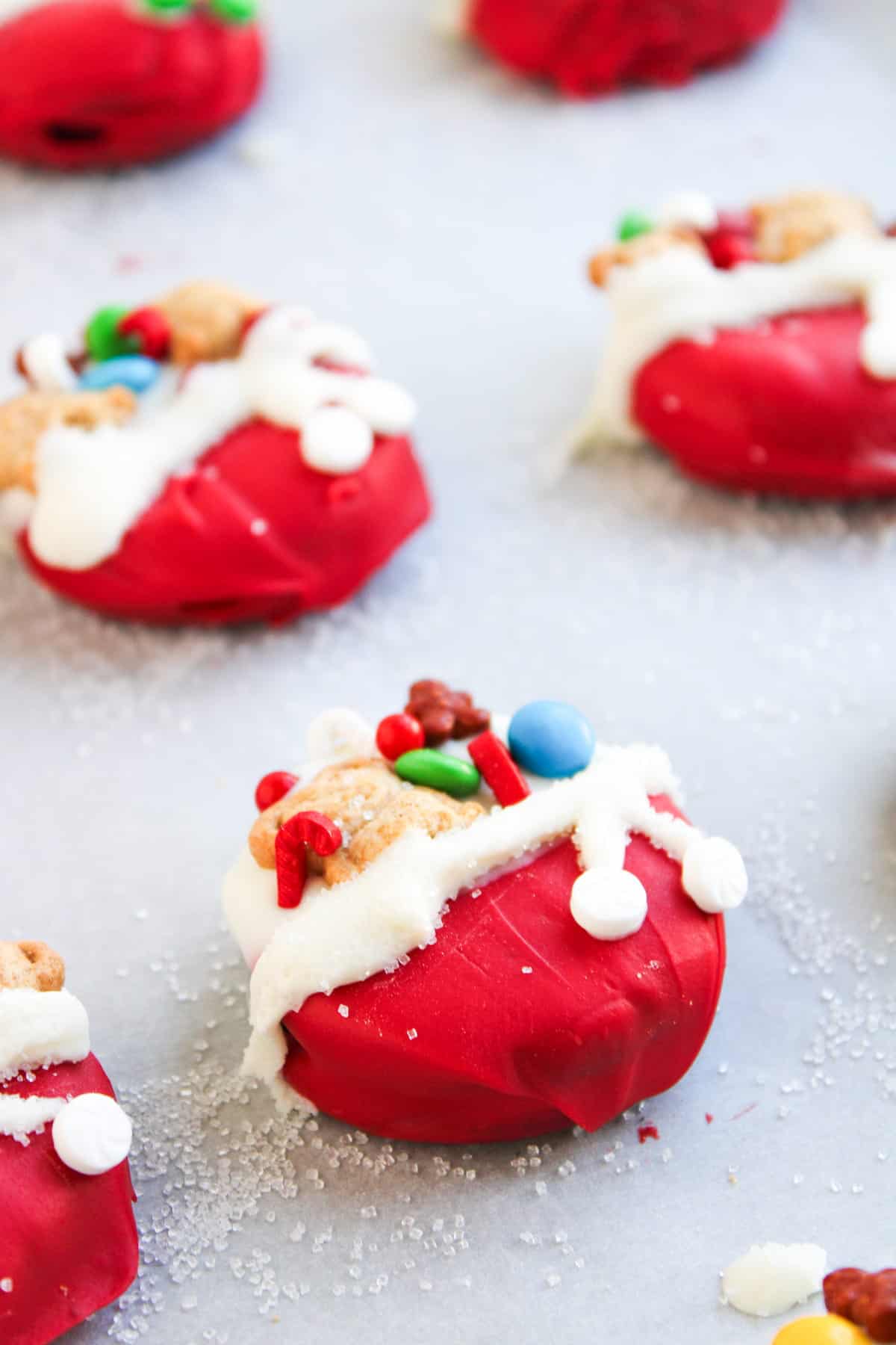 Round cookies coated in red icing, decorated with white icing, sprinkles, and candies to resemble Christmas toy bag, displayed on a white surface.