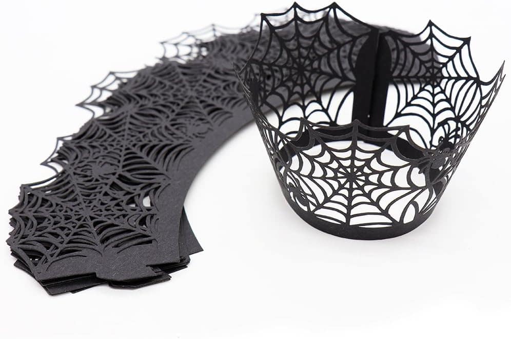 Black paper cupcake wrappers with spiderweb designs, one assembled and others stacked flat on a white background.