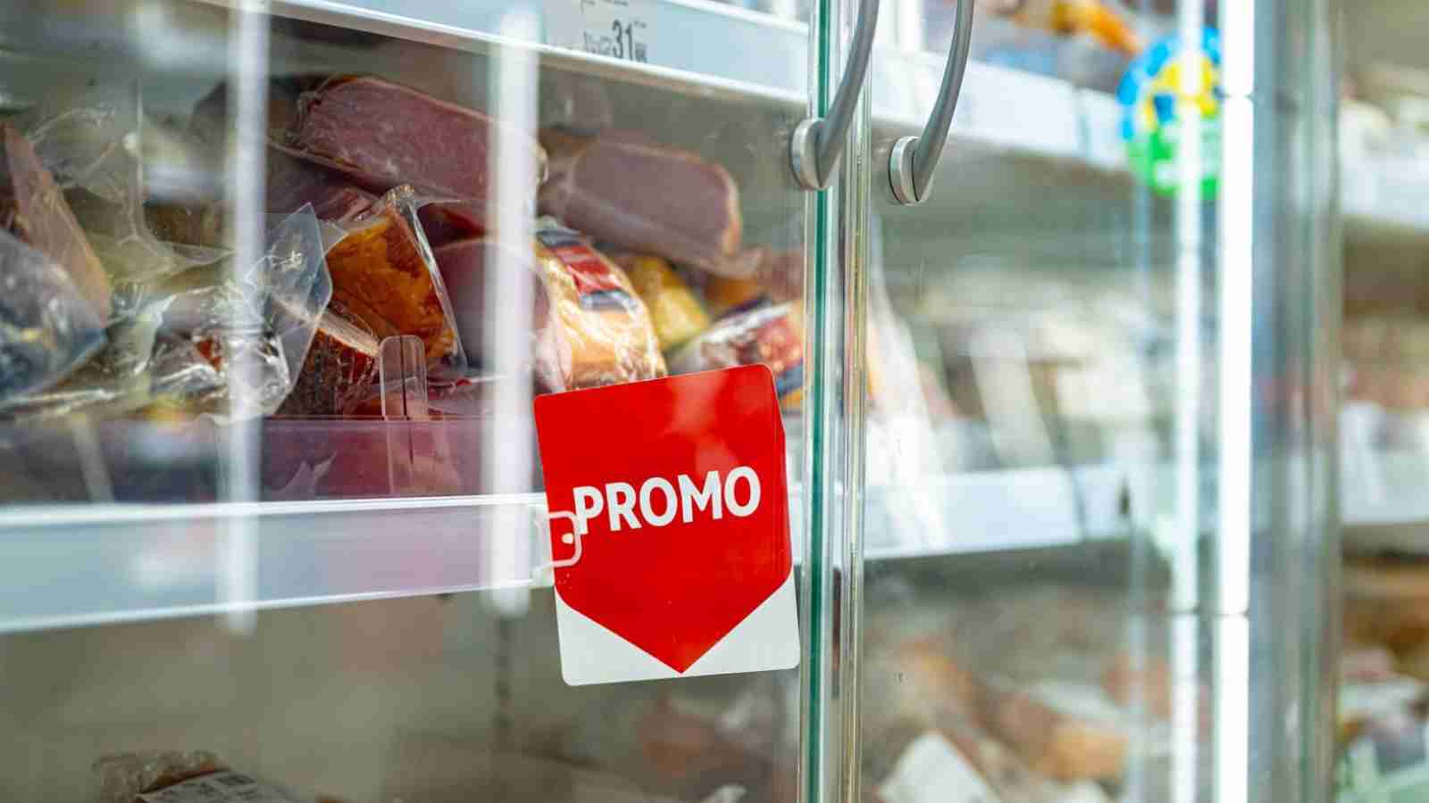 A grocery store freezer with packaged meat inside and a red "PROMO" sign on the glass door.