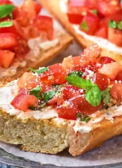 Three slices of toasted bread topped with a tomato mixture, herbs, and grated cheese are arranged on a round plate lined with parchment paper.