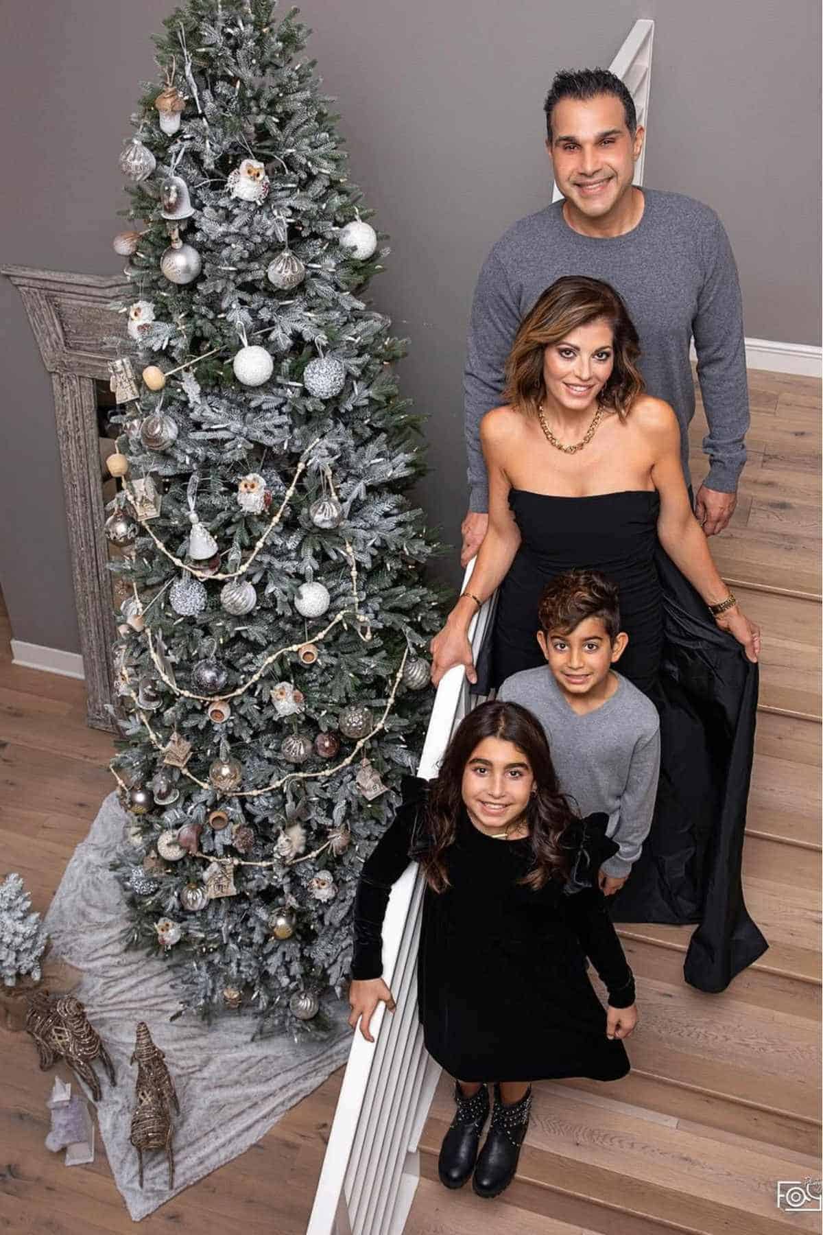 A family of four poses on a staircase next to a decorated Christmas tree in a living room.