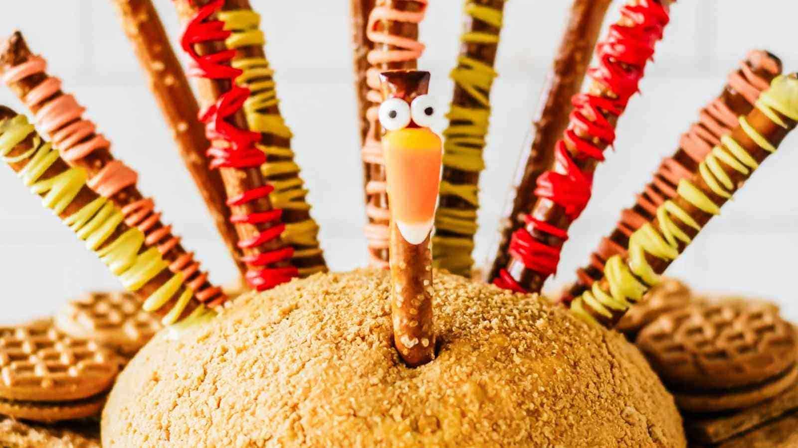 A dessert shaped like a turkey, with a cookie base, pretzel stick feathers decorated with colored icing, and a pretzel stick head with candy eyes and a beak.