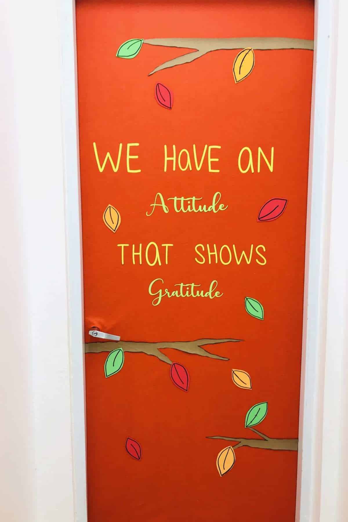 A door decorated with orange paper, fall leaves, and branches, displaying the message: "We have an attitude that shows gratitude.