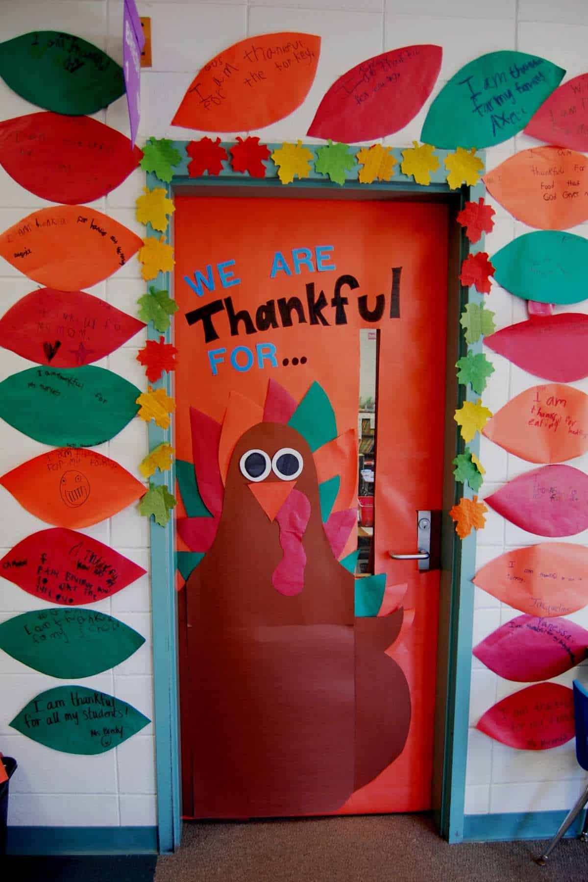 A classroom door decorated with a large paper turkey and colorful paper leaves, each displaying notes of thankfulness written by students.