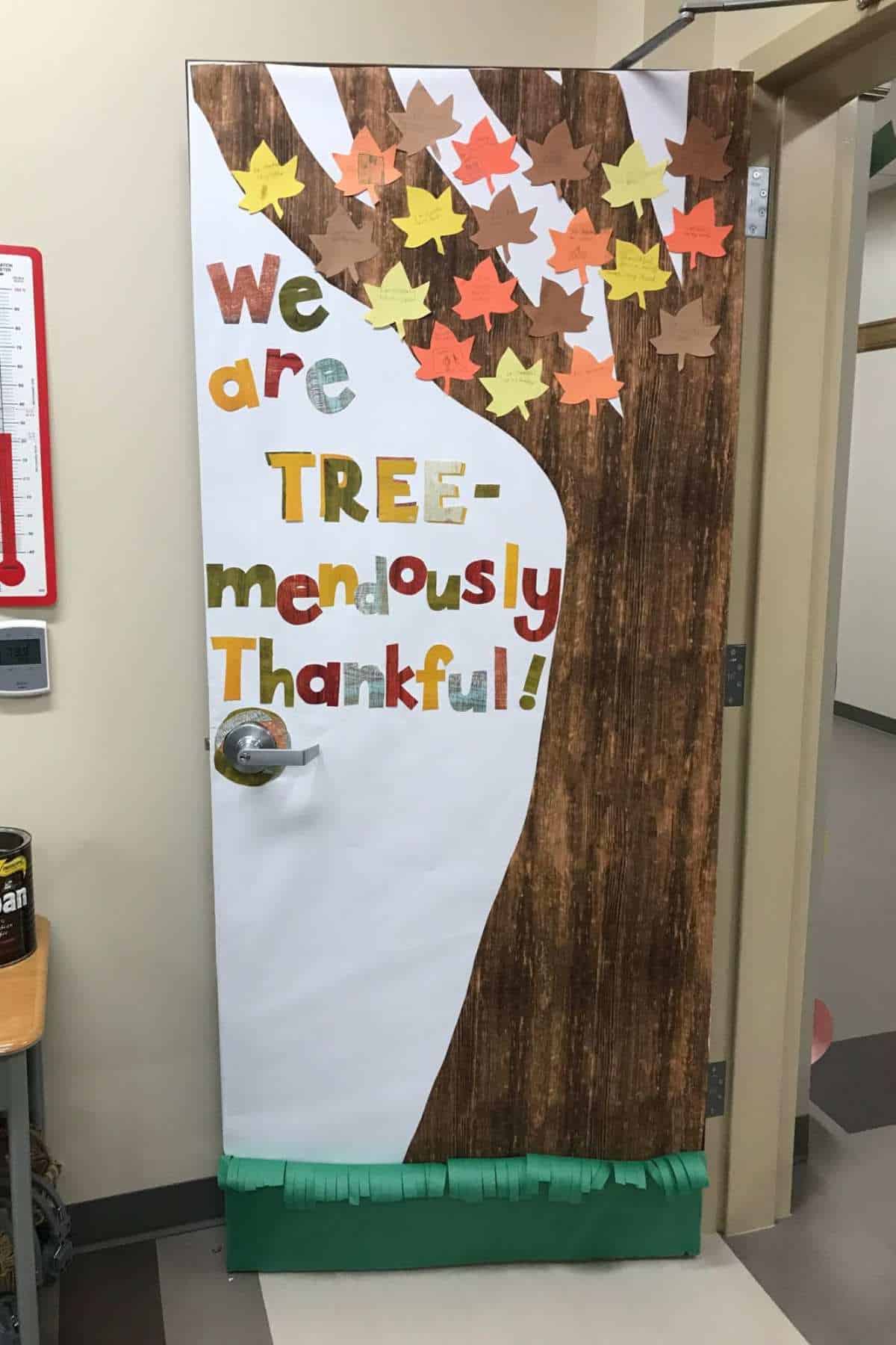 A classroom door decorated with a tree, colored paper leaves, and the words "We are TREEmendously Thankful!" displayed on white paper.