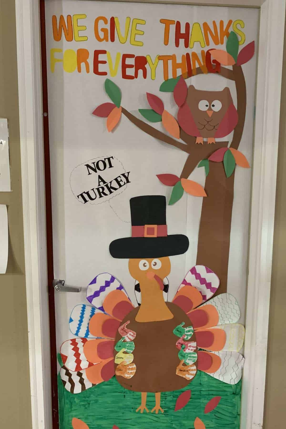 A decorated door features a cartoon turkey wearing a pilgrim hat, a tree with an owl, colorful leaves, and the words "We Give Thanks For Everything" and "Not A Turkey.