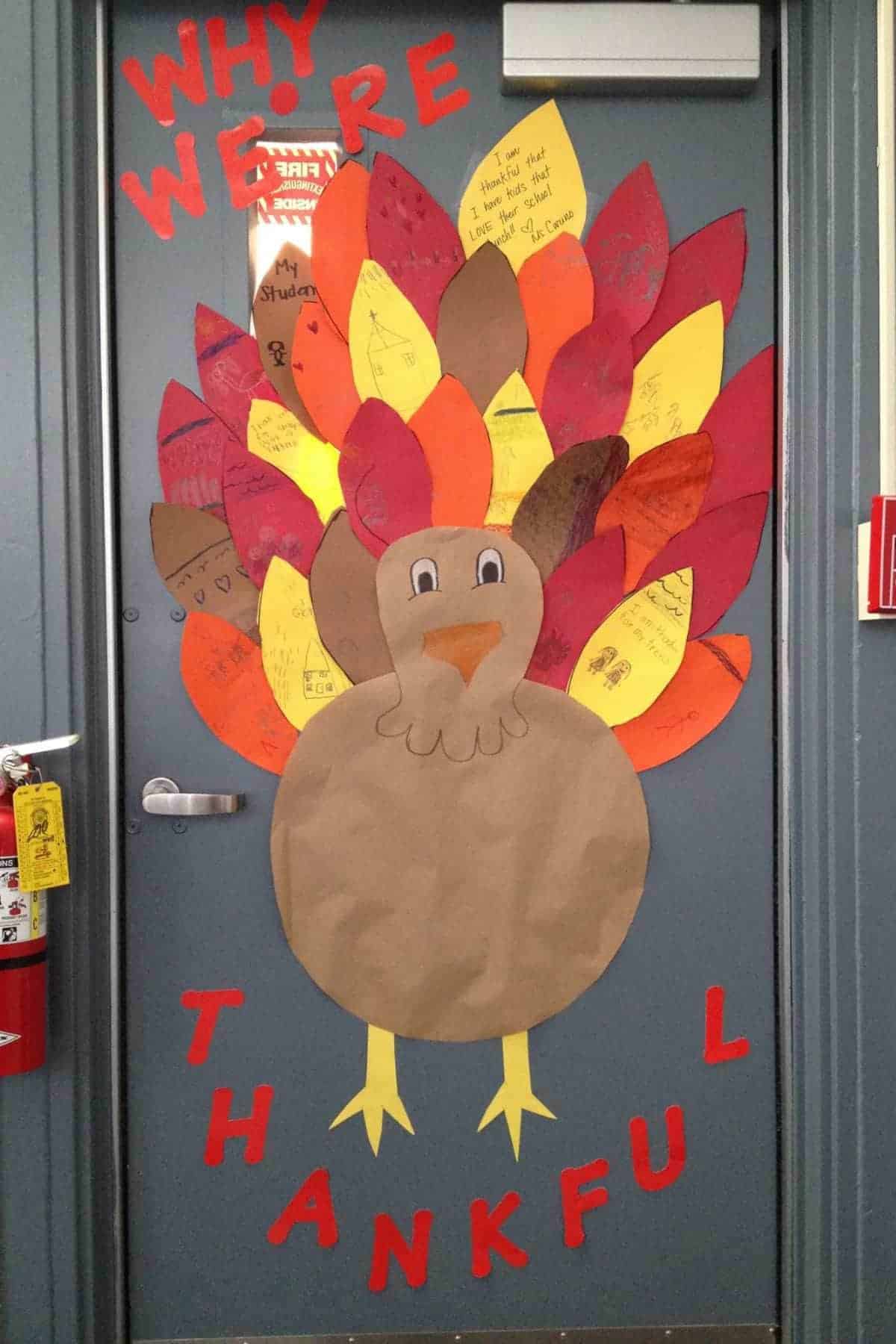 A classroom door decorated with a large paper turkey and colorful feathers, each with handwritten messages about thankfulness; the words "Why We’re Thankful" are displayed above and below.