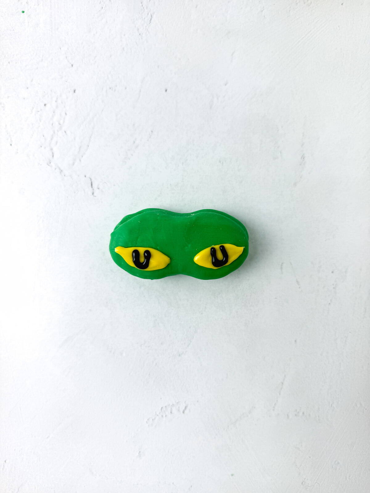 A green nutter butter with two yellow eyes featuring black pupils, on a white textured surface.