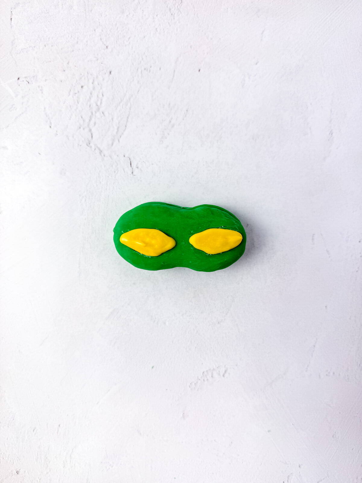 A nutter butter coasted in green chocolate with two yellow oval shapes on top, placed on a light textured surface.