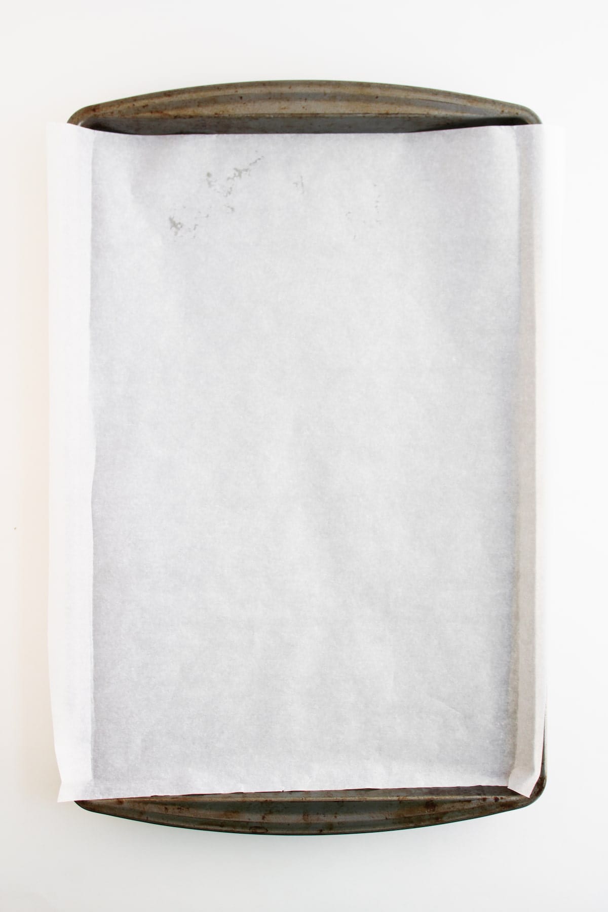 A metal baking sheet lined with a sheet of white parchment paper, photographed from above on a white background.