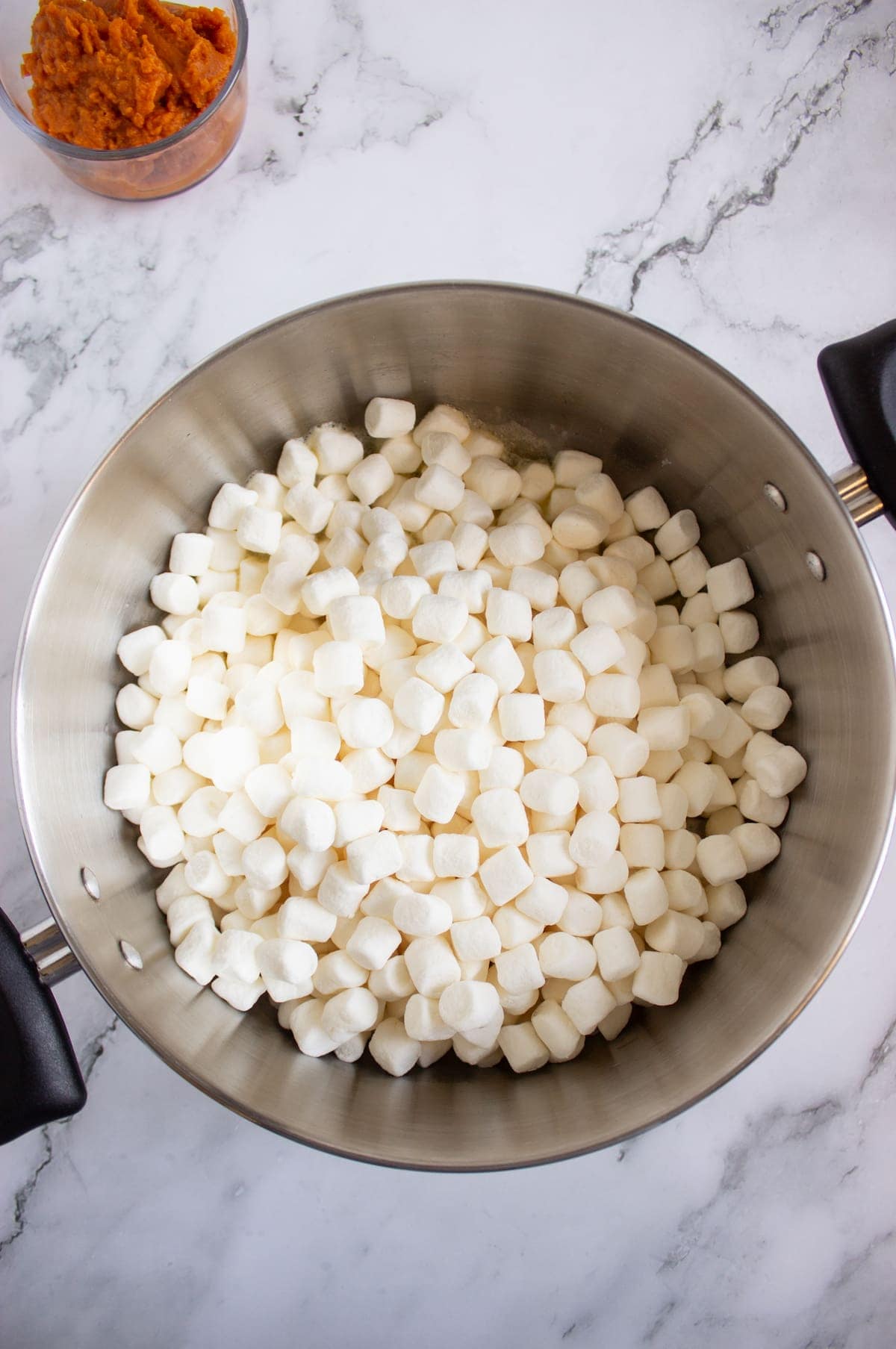 A large pot filled with mini marshmallows sits on a marble countertop; a small container of mashed sweet potatoes is visible in the corner.