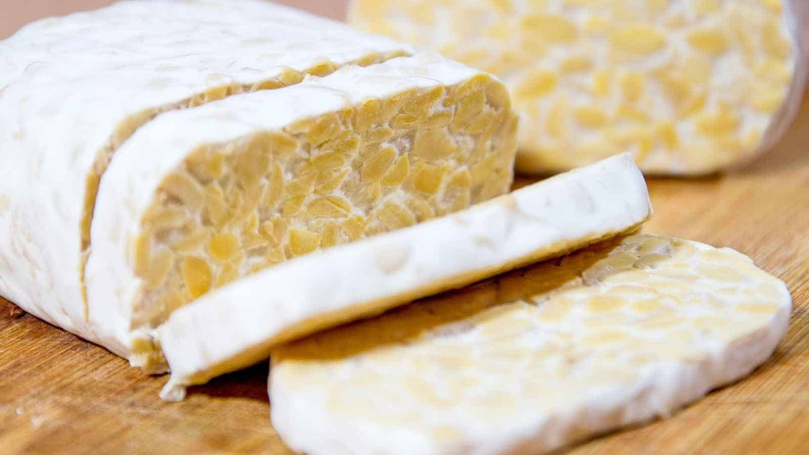 Close-up of sliced tempeh on a wooden cutting board, showing the texture of the fermented soybean product.
