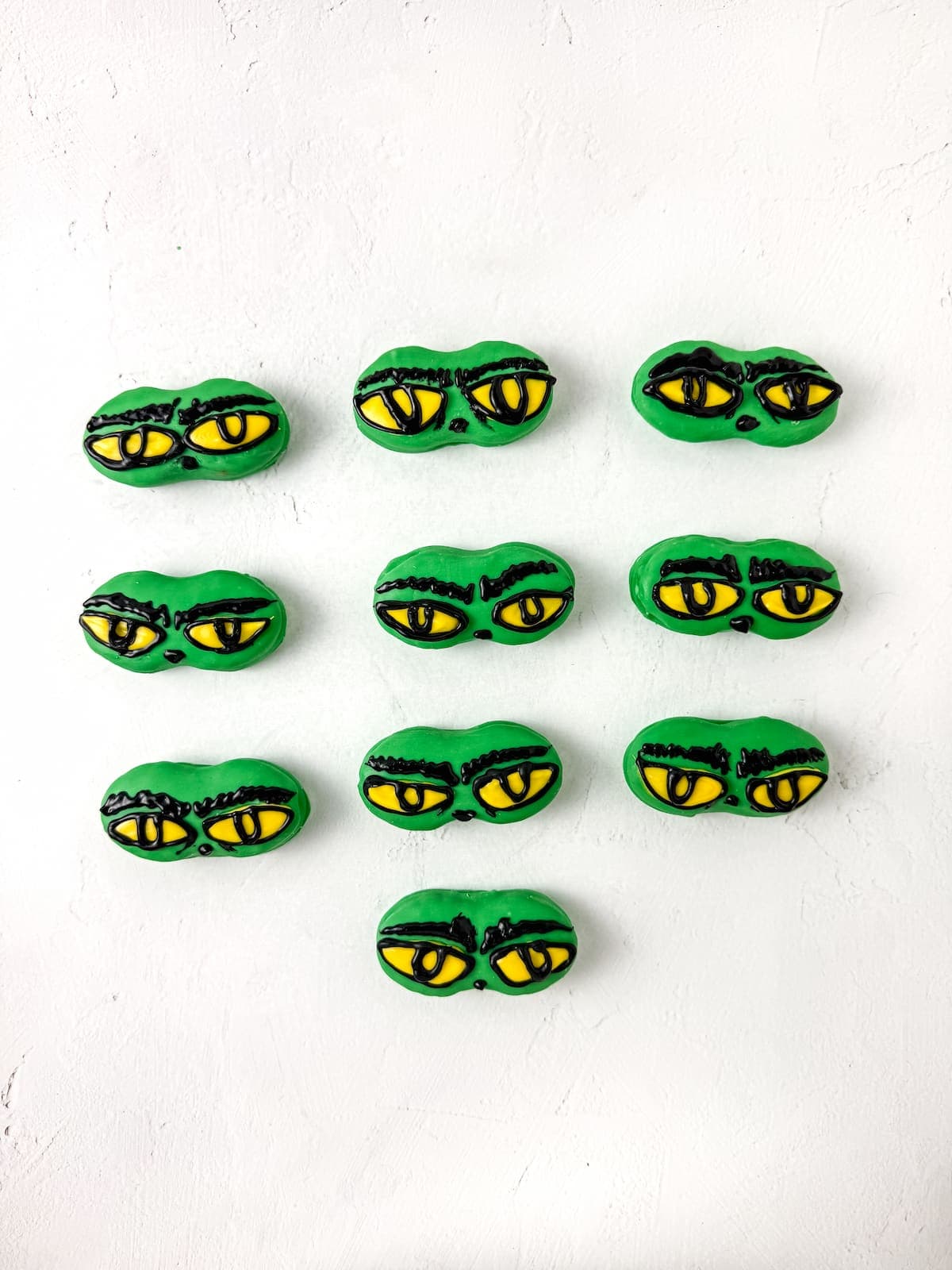 Ten nutter butter cookies decorated with yellow and black eyes are arranged in a grid pattern on a white background.