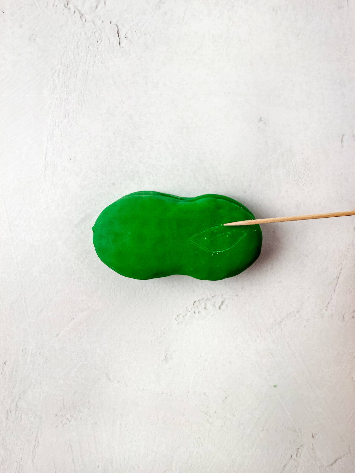 A nutter butter in a smooth surface is being touched by a wooden stick on a light textured background.