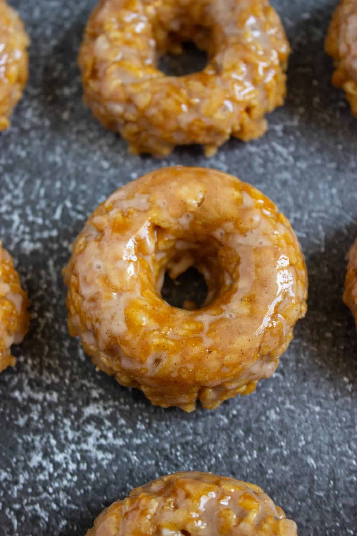 Close-up of several glazed old fashioned donuts arranged on a dark, textured surface.
