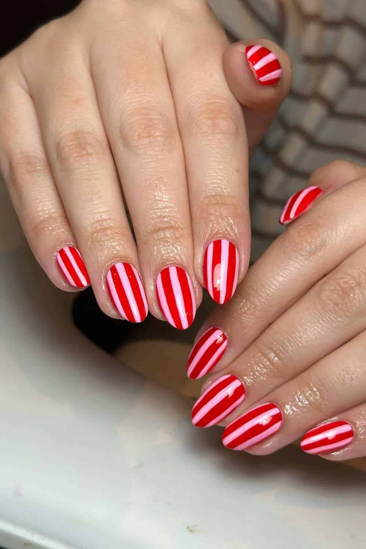 Close-up of hands with red and white vertical striped nail art.