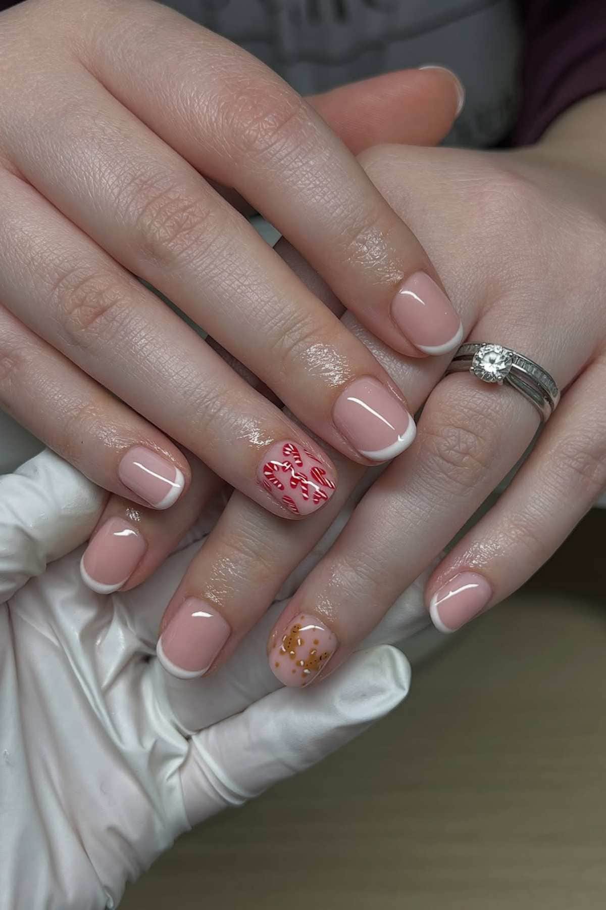 A hand with a French manicure, featuring candy cane art on one ring finger and gold dots on the other, held by a gloved hand.