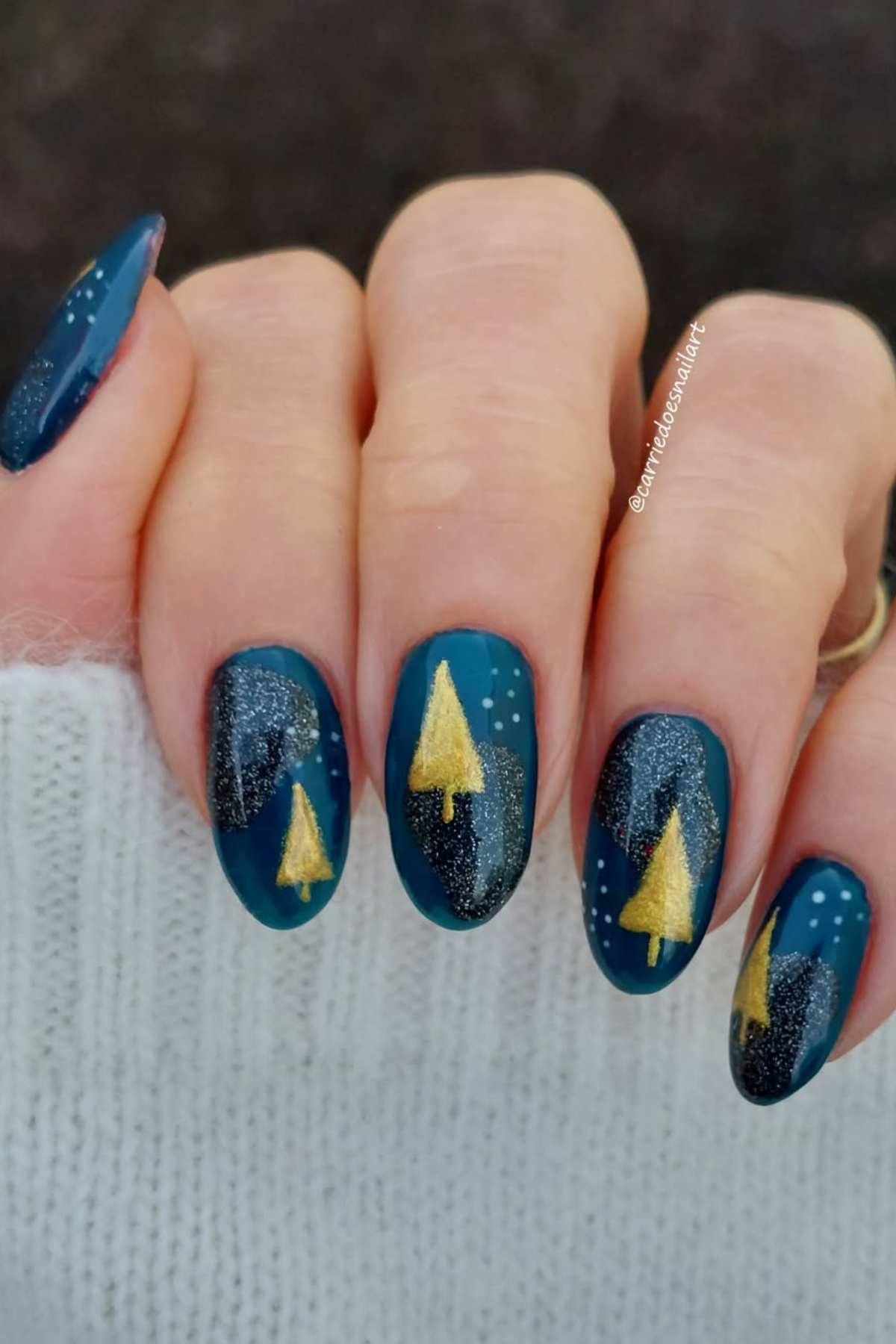 A hand with teal nail polish featuring gold Christmas tree designs and silver glitter accents on each nail.