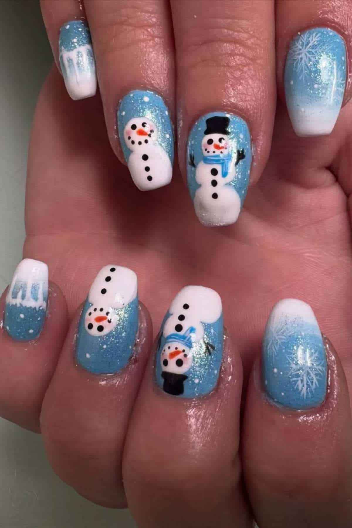 A hand with blue and white winter-themed nail art featuring snowmen and snowflakes on each fingernail.