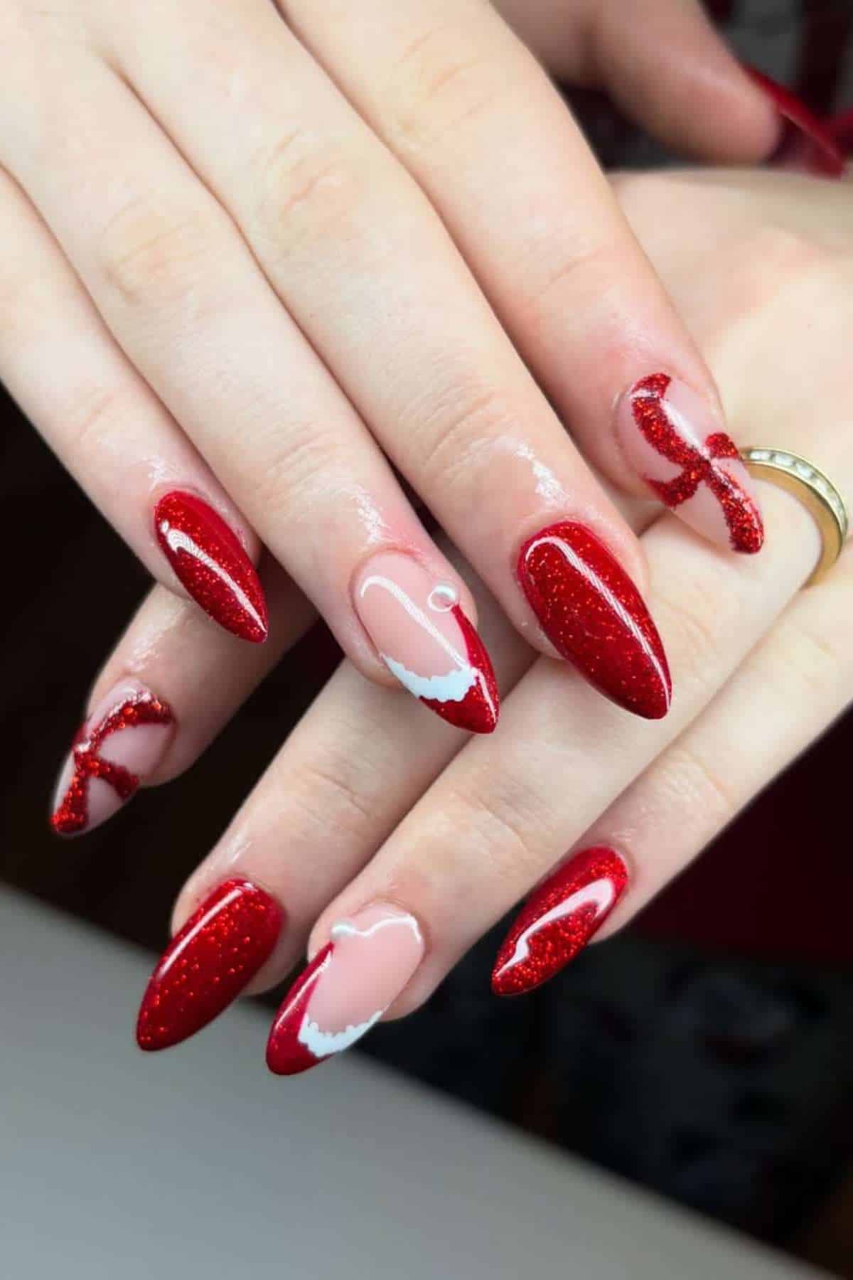 Hands with long, almond-shaped nails painted in red with glitter; some nails feature pink accents and abstract white and red designs.