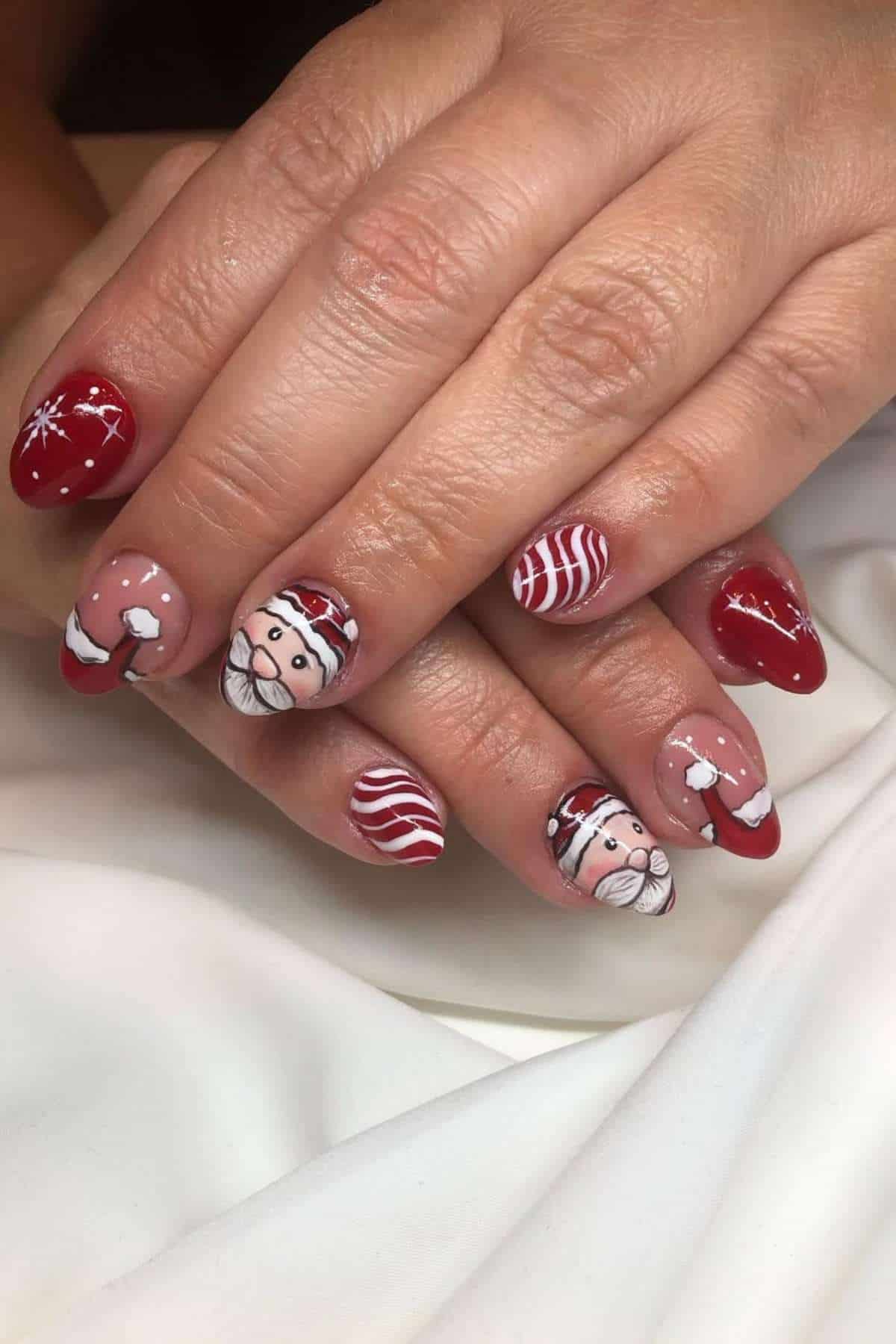 Hands with red and white Christmas-themed nail art, featuring Santa Claus faces, candy cane stripes, and snowflakes on fingernails.