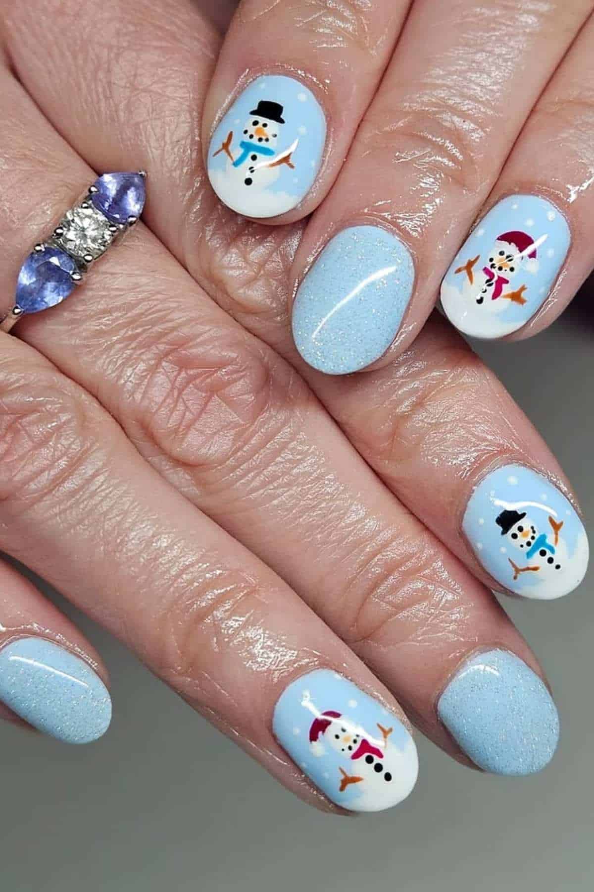 Close-up of hands with light blue glittery nail polish featuring snowman designs on select nails.