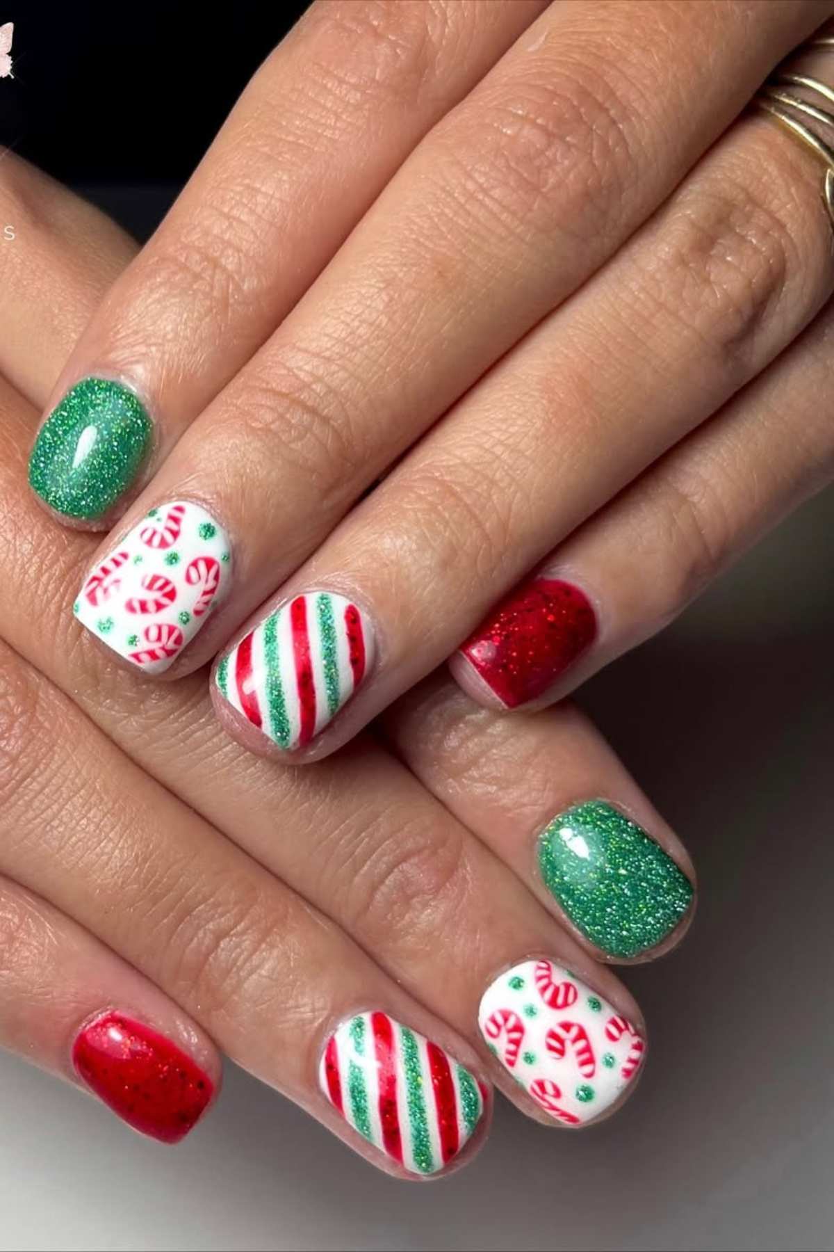 Hands with festive nail art featuring green glitter, red polish, white bases with red and green stripes, and candy cane designs.