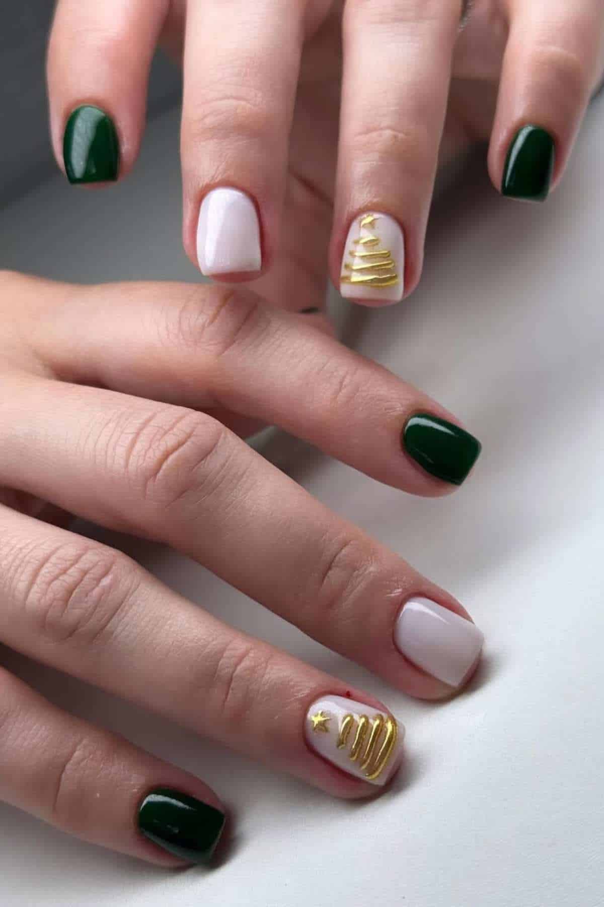 A hand with nails painted green and white; two white nails feature gold Christmas tree designs.