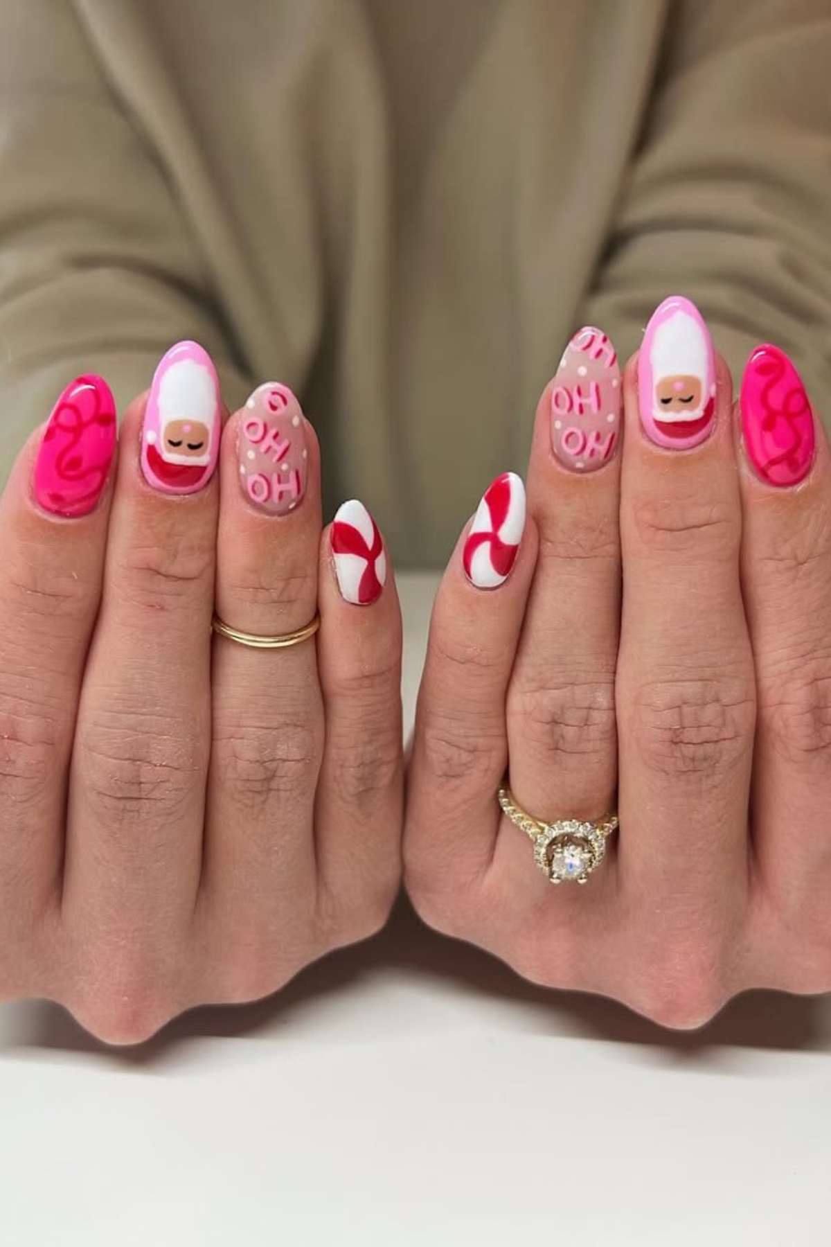 Two hands with long nails featuring pink, red, and white designs, including swirls, "O H" letters, and smiley faces. The person wears a gold ring and a diamond ring.