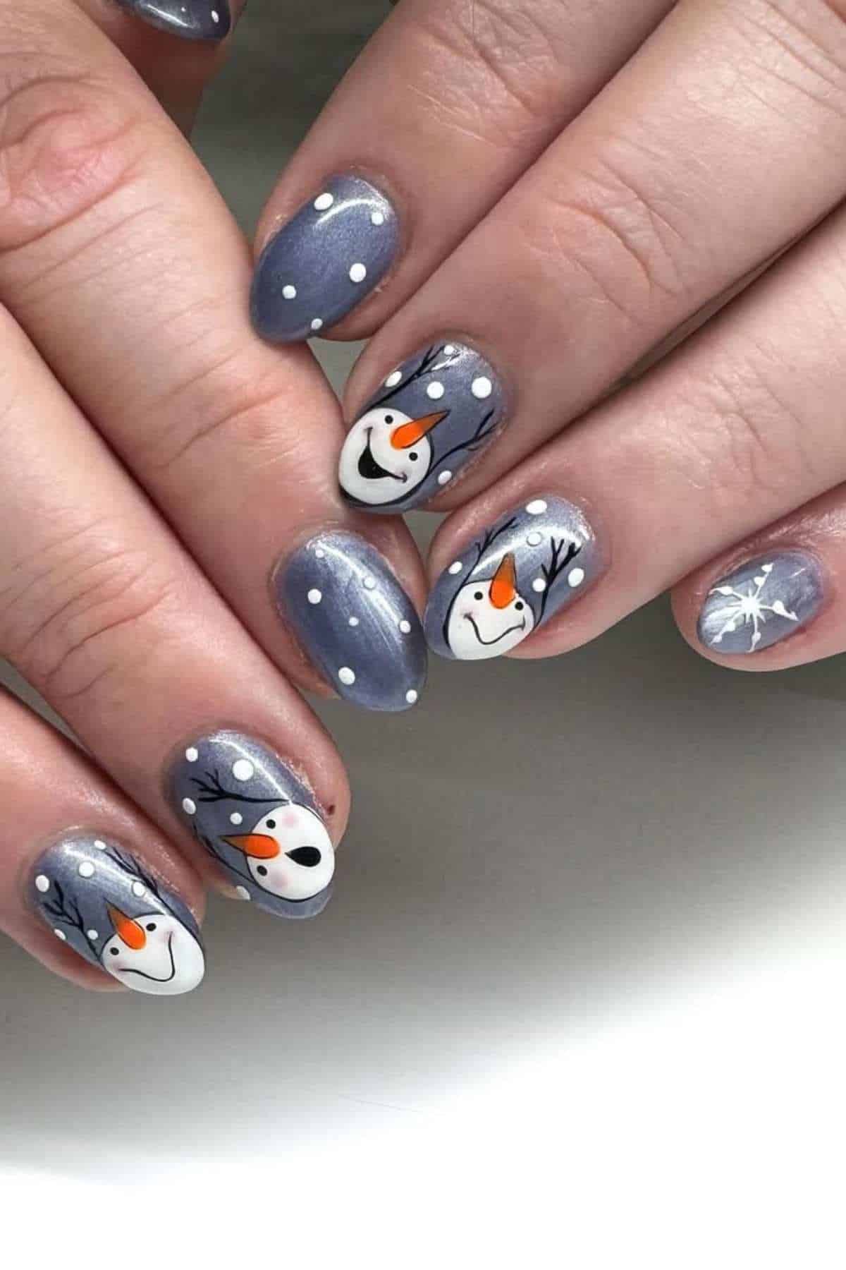 Fingernails painted gray with white dots, featuring snowman faces and tree branch designs as winter-themed nail art.