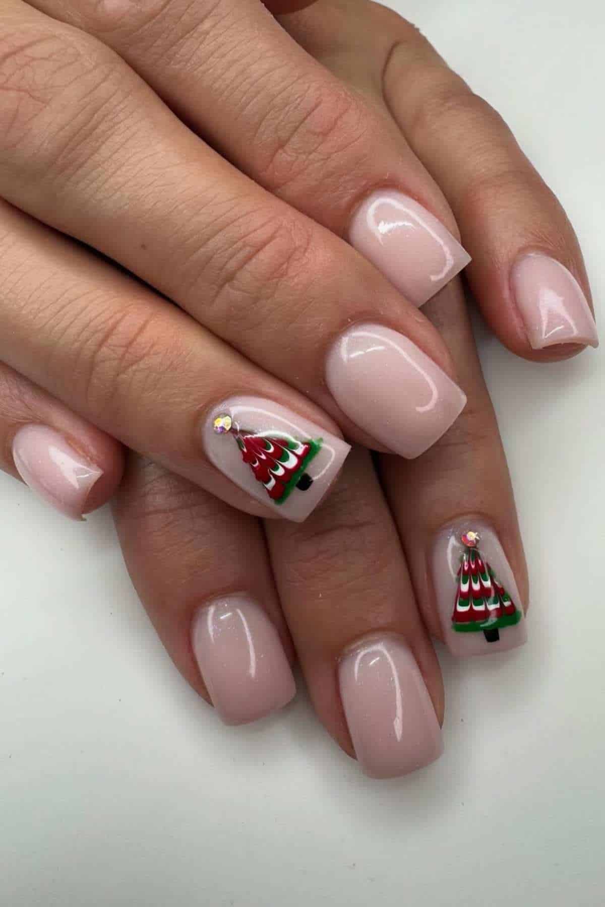 Hands with short, square, pale pink nails; ring and thumbnail on each hand feature a small Christmas tree design with a rhinestone star on top.