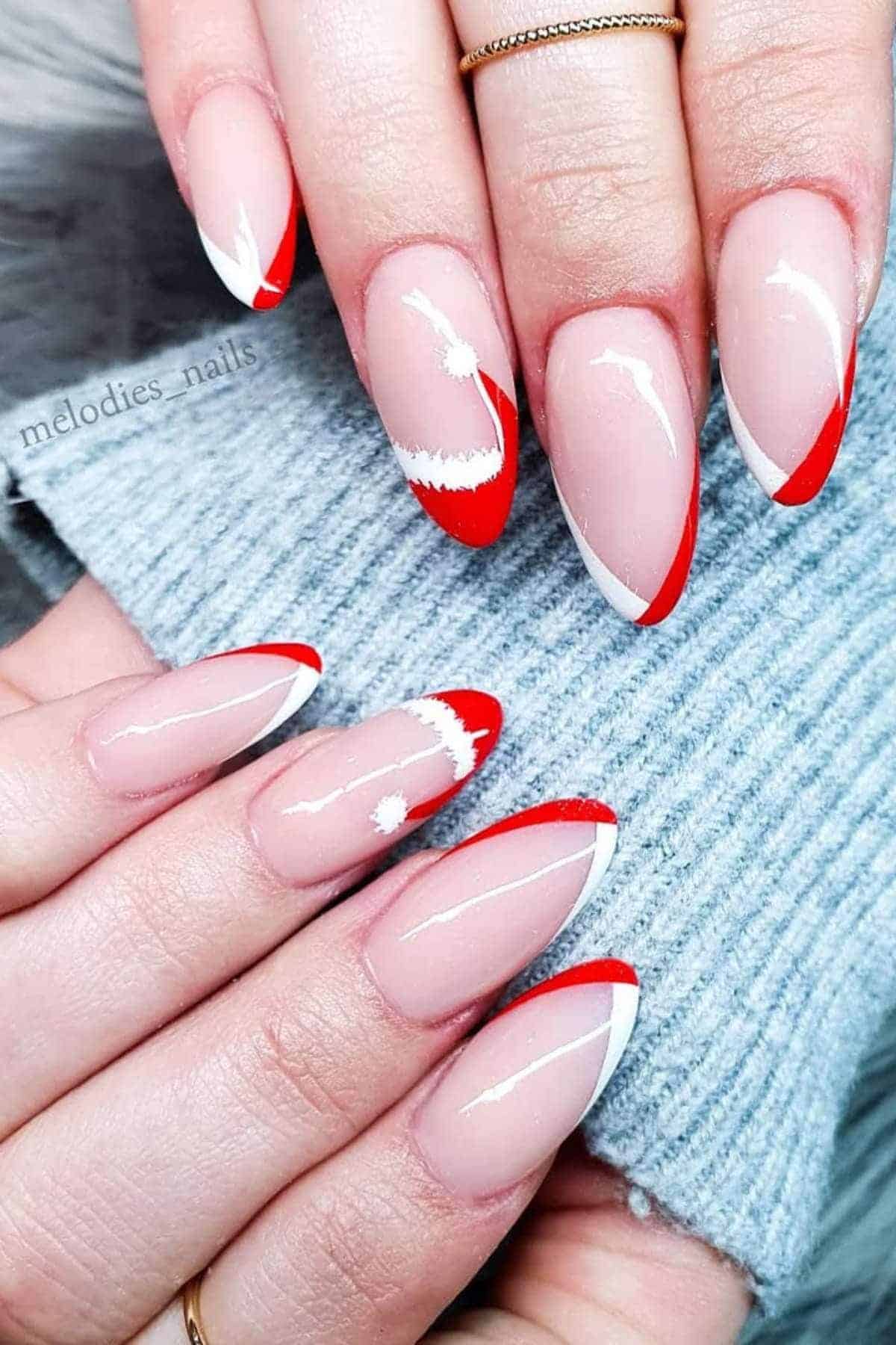 Close-up of hands with almond-shaped nails featuring a nude base, red and white tips, and minimal white abstract designs on two nails.