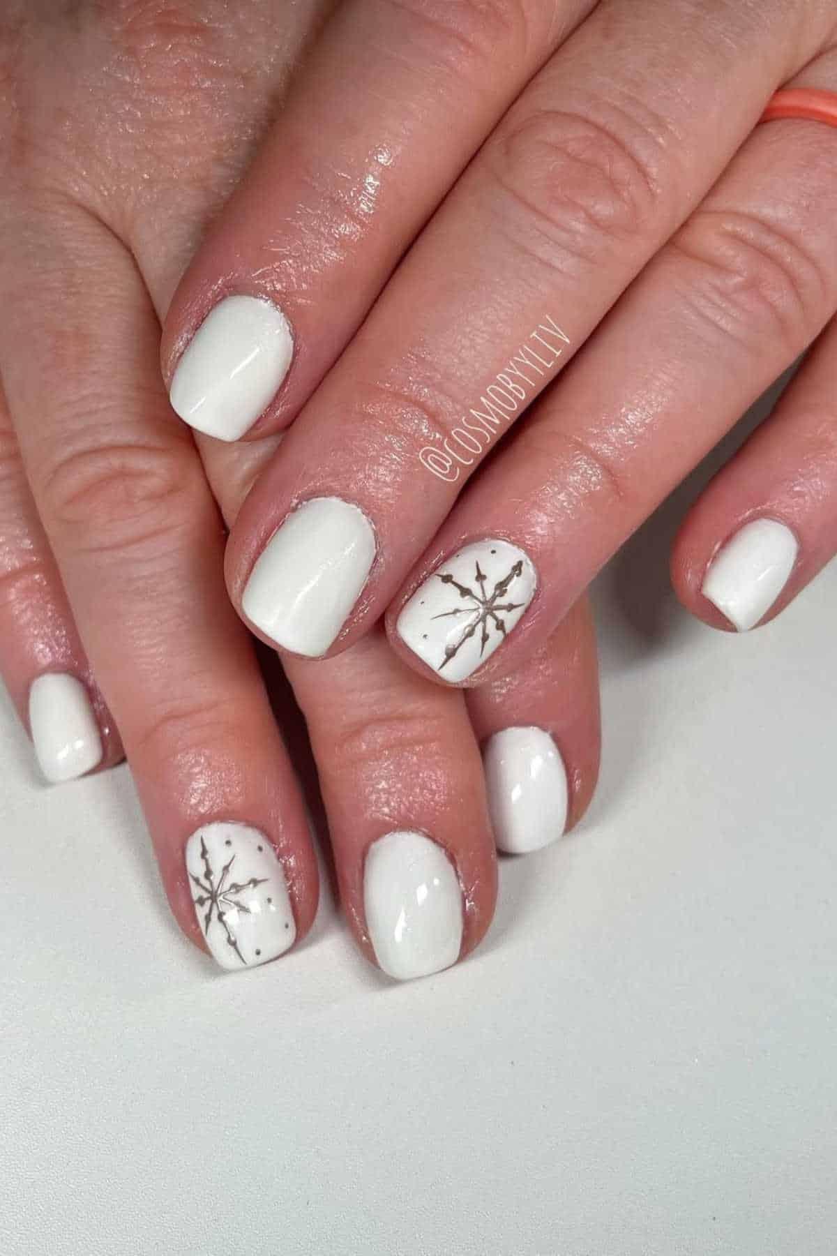 Hands with short, neatly manicured nails painted white; two nails feature silver snowflake designs as accents.