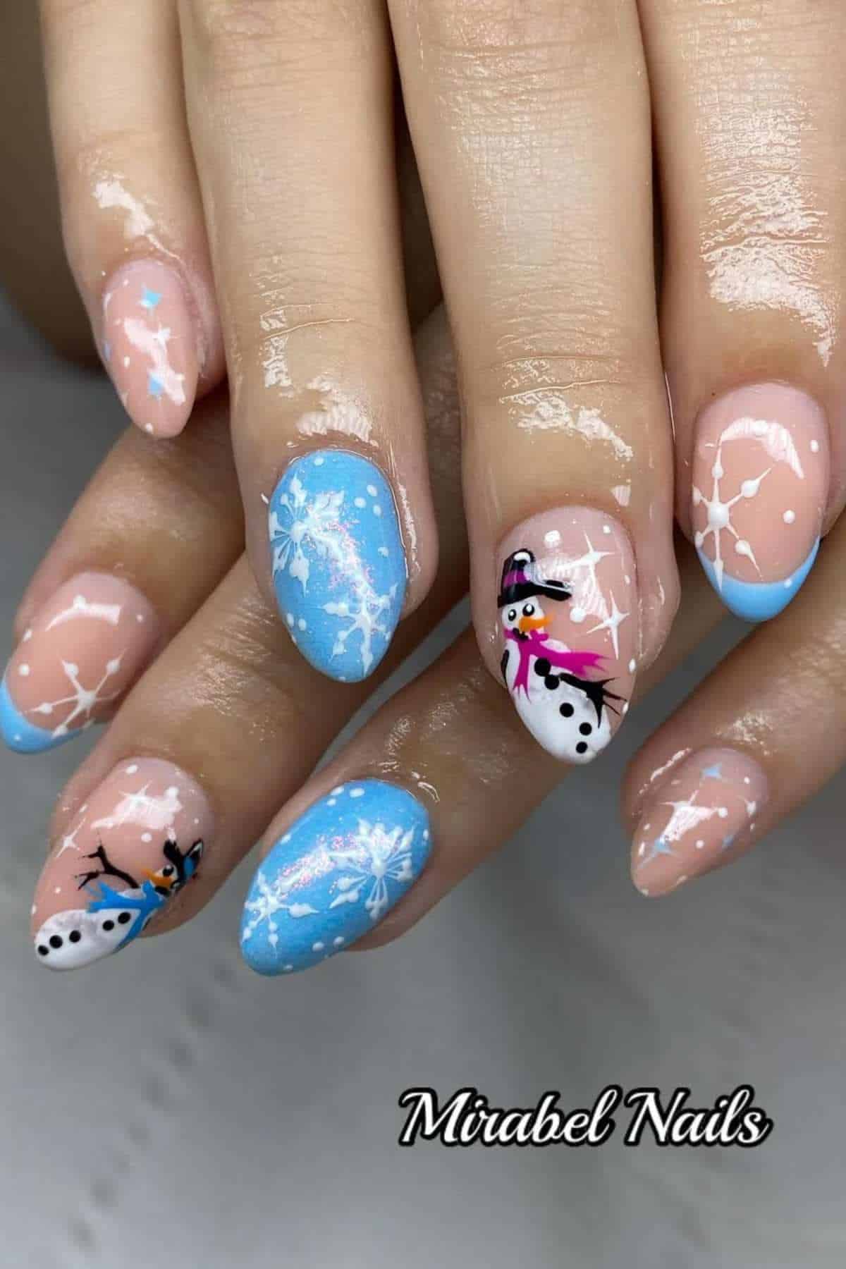 Hands with almond-shaped nails featuring blue and nude French tips, white snowflake designs, and cartoon snowman art on two accent nails. "Mirabel Nails" text appears at the bottom.