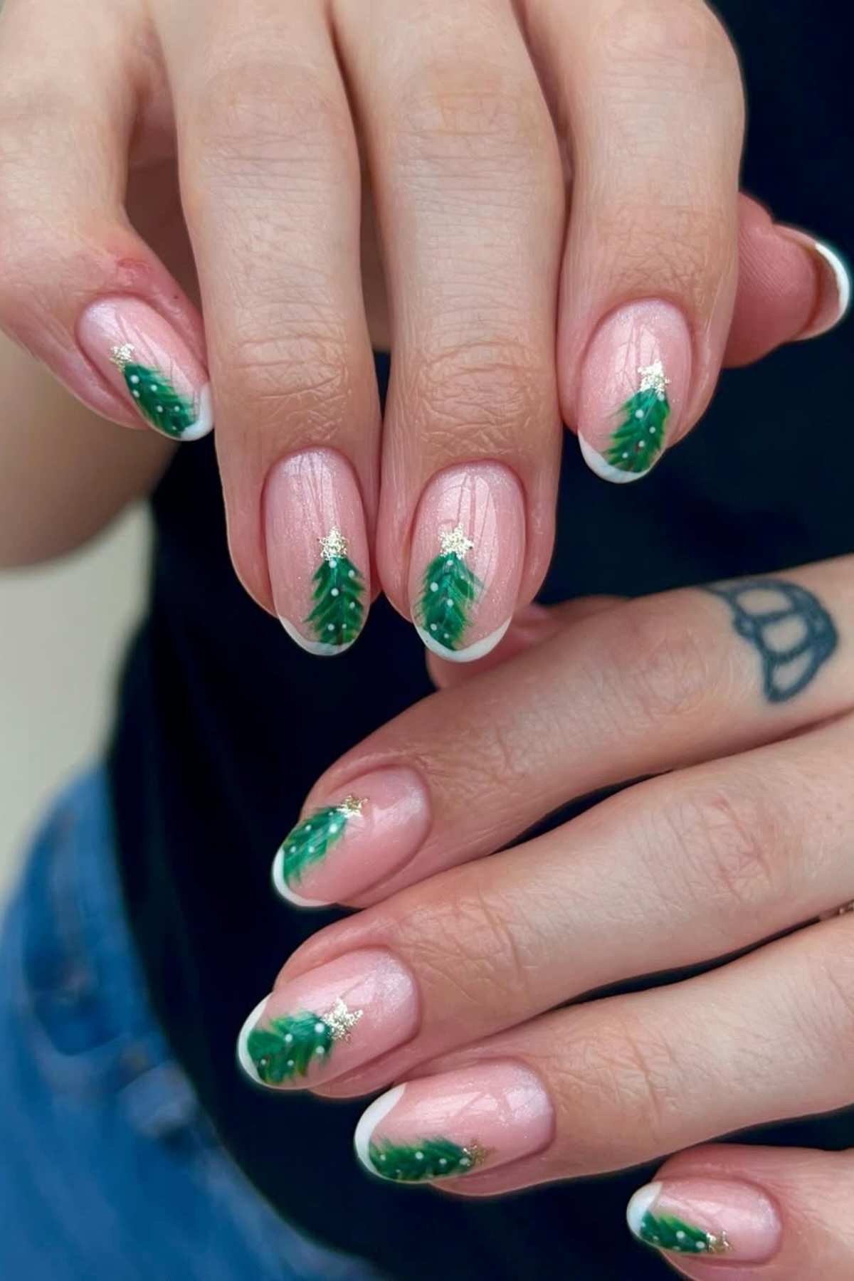 Close-up of hands with light pink nails featuring green Christmas tree designs at the tips, decorated with small white stars.