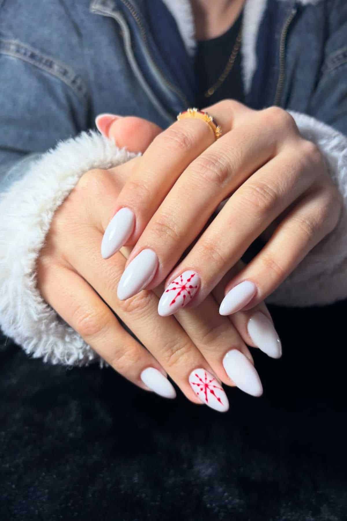 Hands with long, almond-shaped white nails; the ring finger on each hand features a red snowflake design.