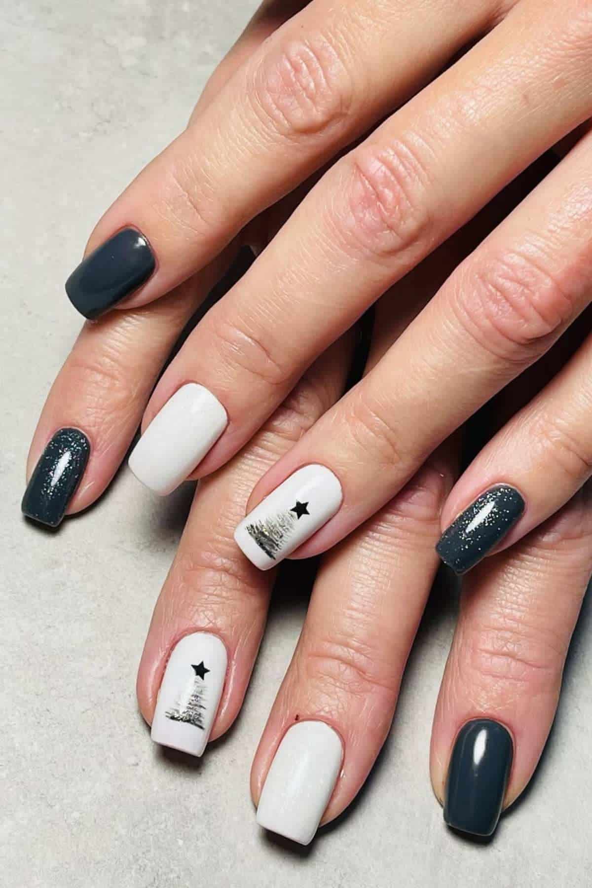 Close-up of hands with manicured nails, featuring a mix of dark grey, white, and accent nails with black star and tree designs.