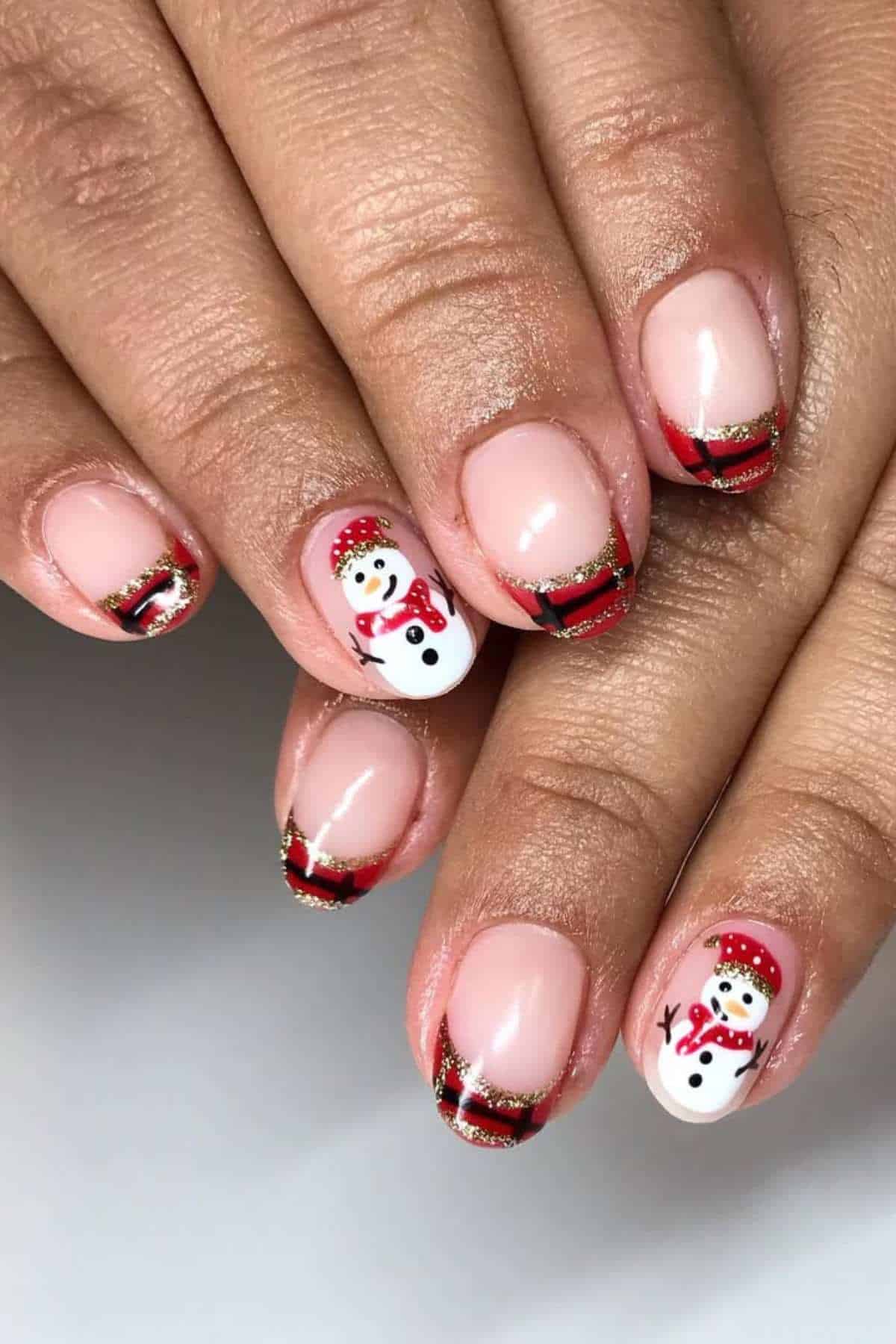 Fingernails with a red and gold tipped French manicure design, featuring snowman and ribbon art on two accent nails.