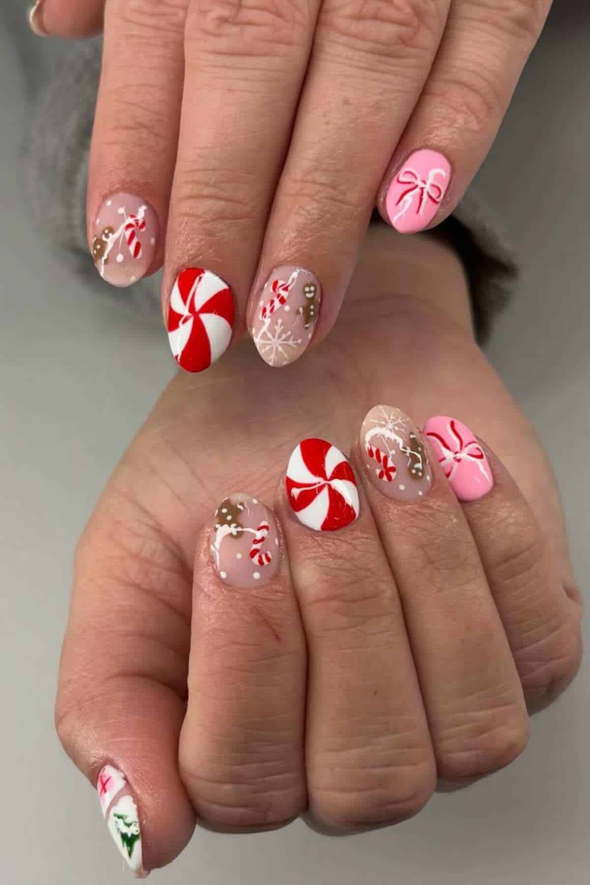 Hands with festive nail art featuring red and white peppermint swirls, pink bows, snowflakes, gingerbread men, and candy designs on almond-shaped nails.