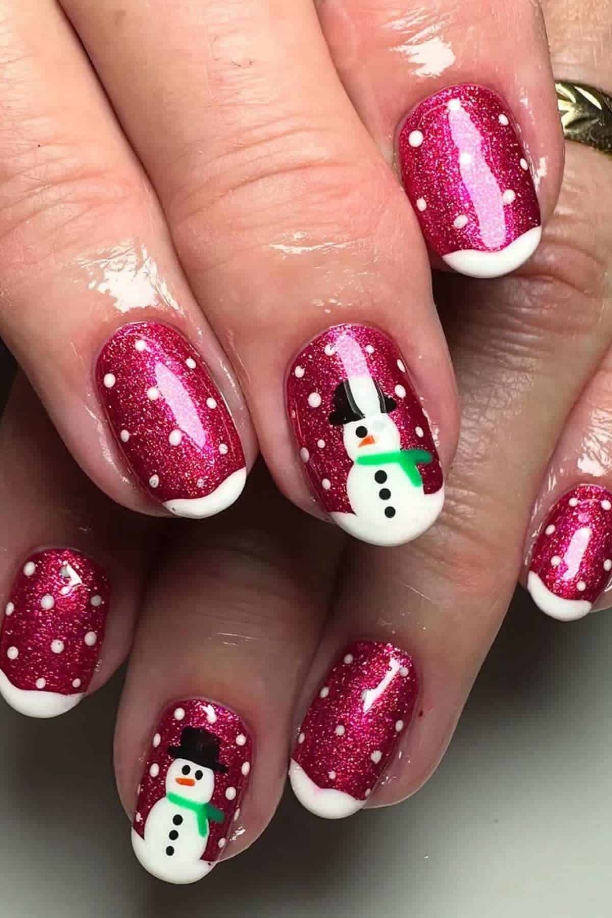 Fingernails painted with red glitter polish, white tips, white dots as snow, and two nails featuring snowman designs with hats, scarves, and buttons.